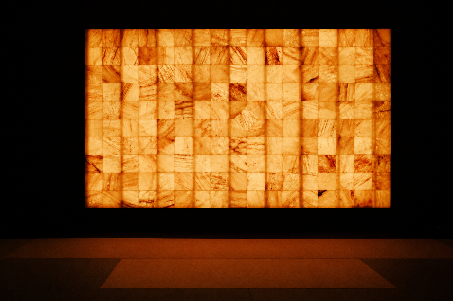 Backlit wall installation made of small orange and white patterned tiles, framed in black, on a dark wall with a tiled floor in foreground.
