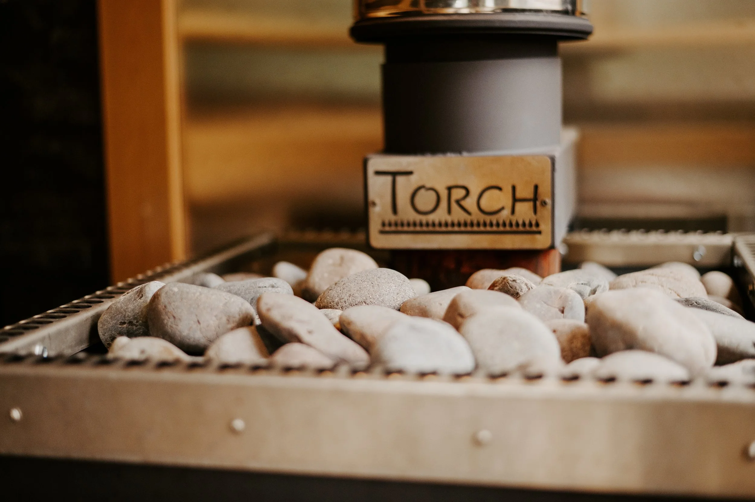Close-up of a small wooden sign with the word 'Torch' on it, placed among smooth white stones on a conveyor belt, with a blurred background.