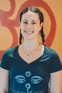 Young woman with braided hair smiling, wearing a dark blue T-shirt featuring an eye and third eye graphic, standing against a decorative orange background.