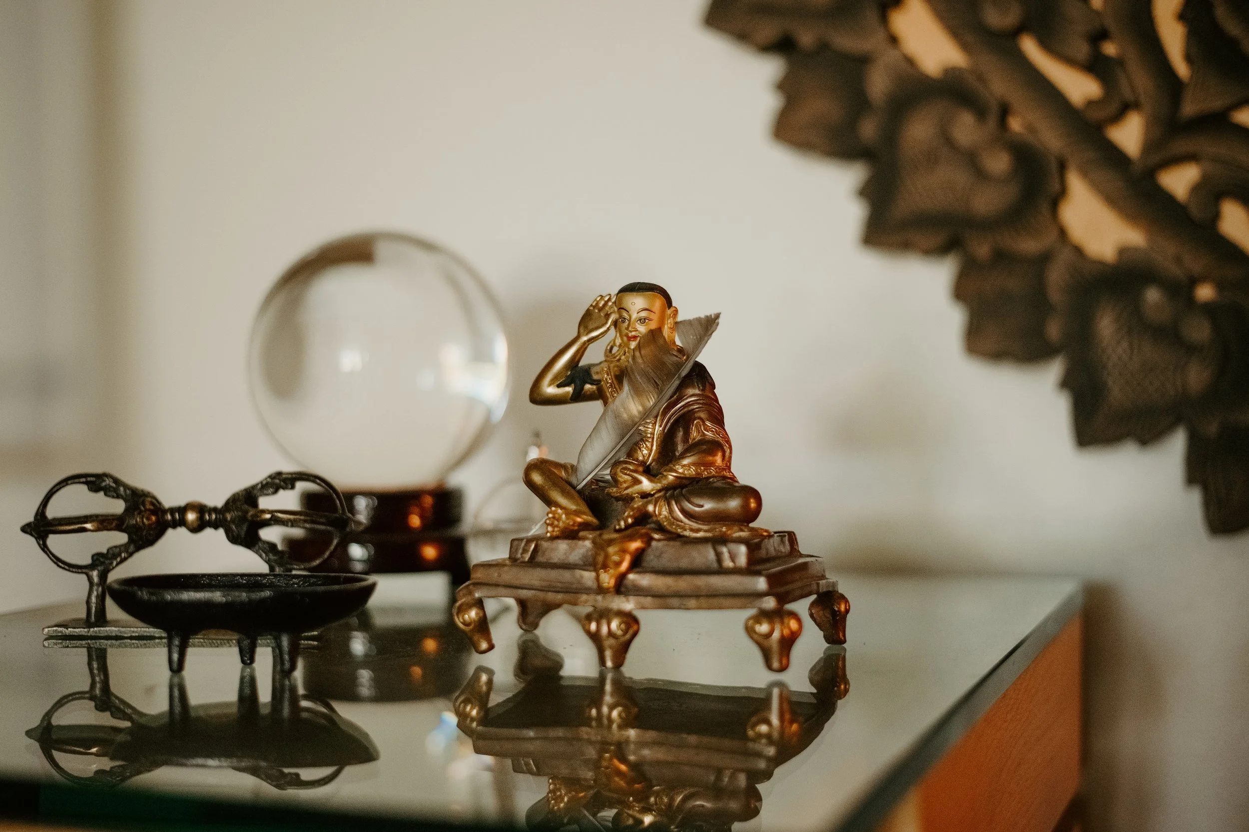 Decorative figurine of a woman sitting with one hand on her head, placed on a glass surface with other ornate objects around.