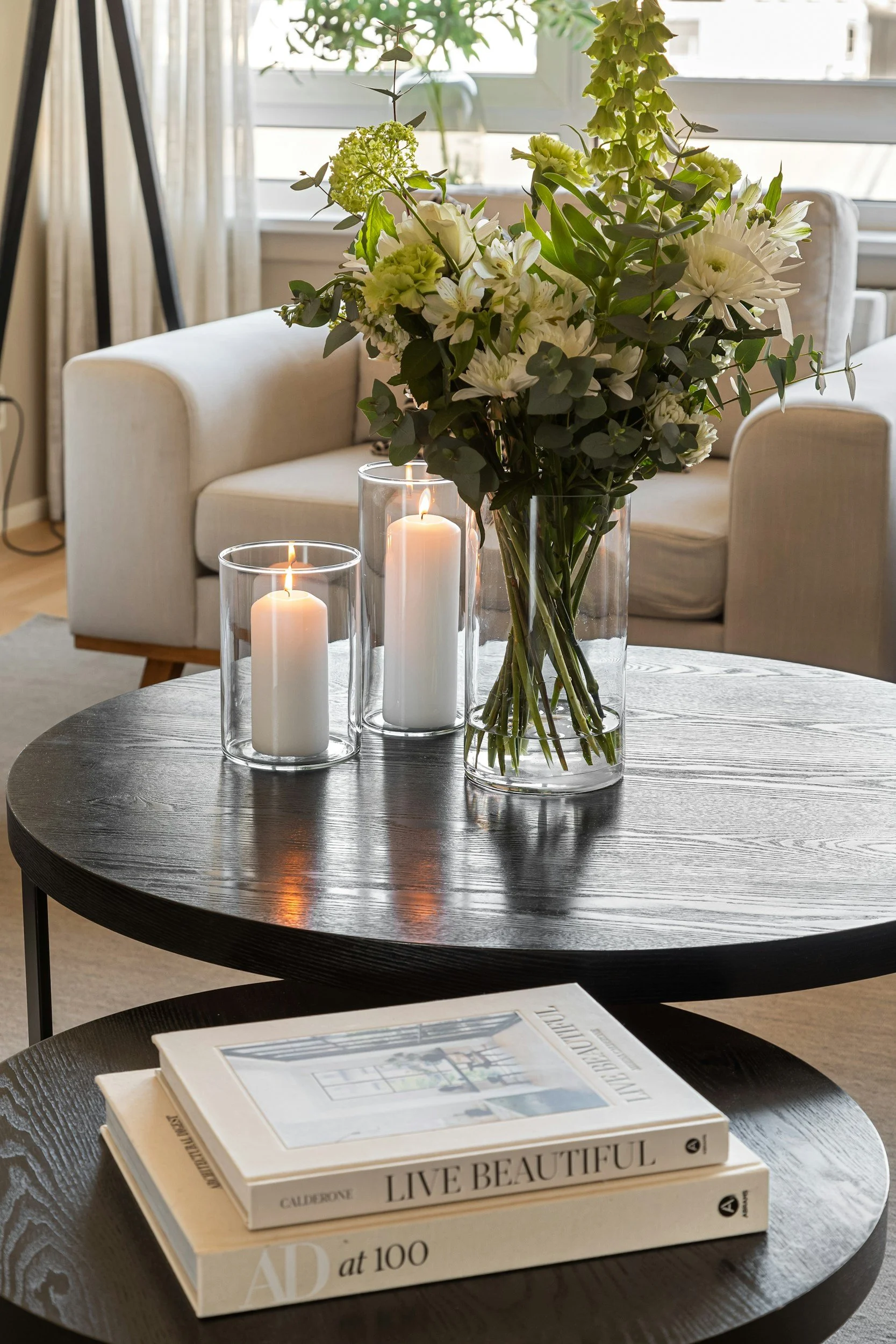 Pillar candles in glass hurricane holders with fresh flowers on a round coffee table
