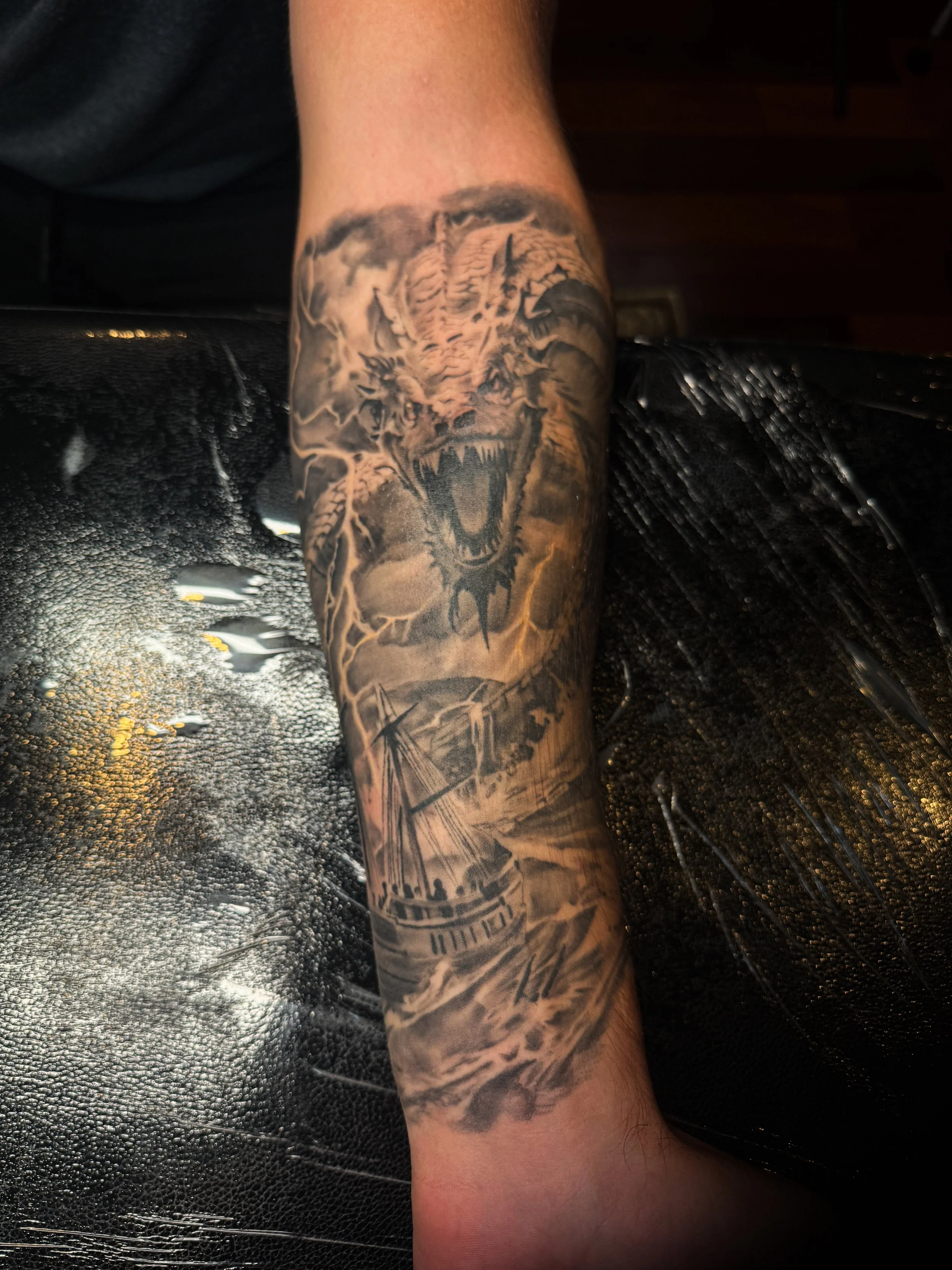 A detailed black and gray tattoo of a roaring serpent on a person's arm, set against a dark background.