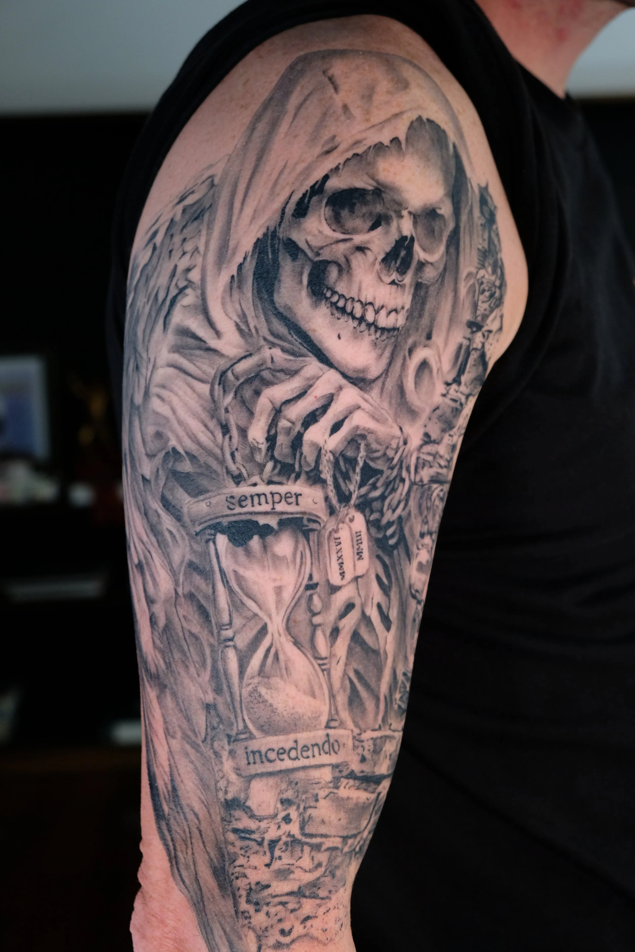 Black and gray tattoo sleeve featuring a detailed skull with a hood, Latin words "semper incendo" on a scroll, and intricate designs throughout.