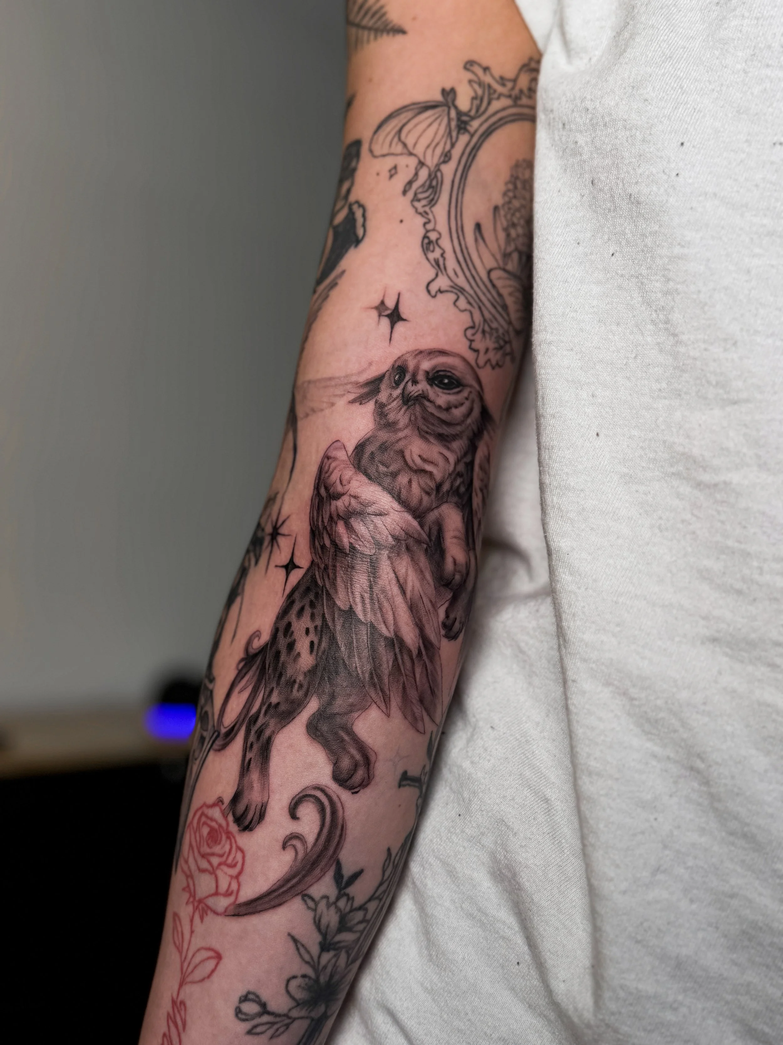 Close-up of a tattoo sleeve featuring an owl, a butterfly, stars, flowers, and decorative patterns on a person's arm.