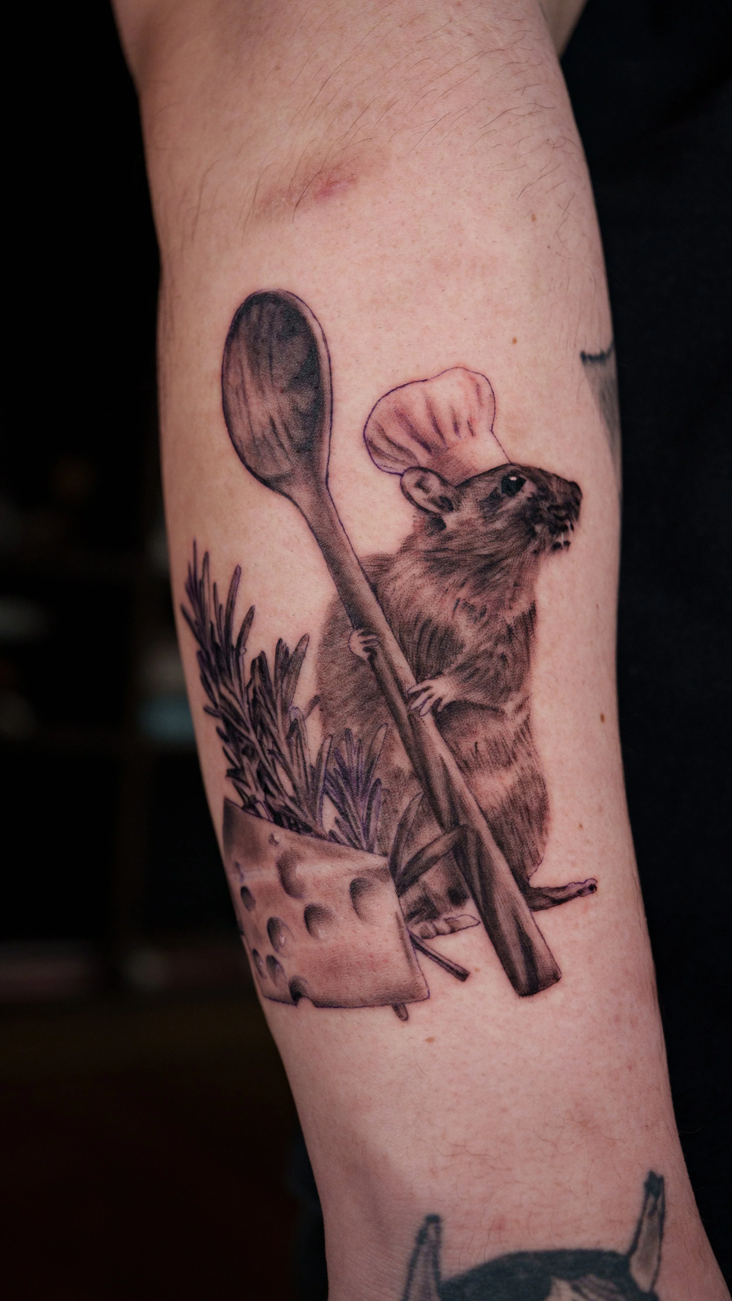 Tattoo of a mouse wearing a chef's hat standing on a plant next to a large spoon, with a small plant in a pot.