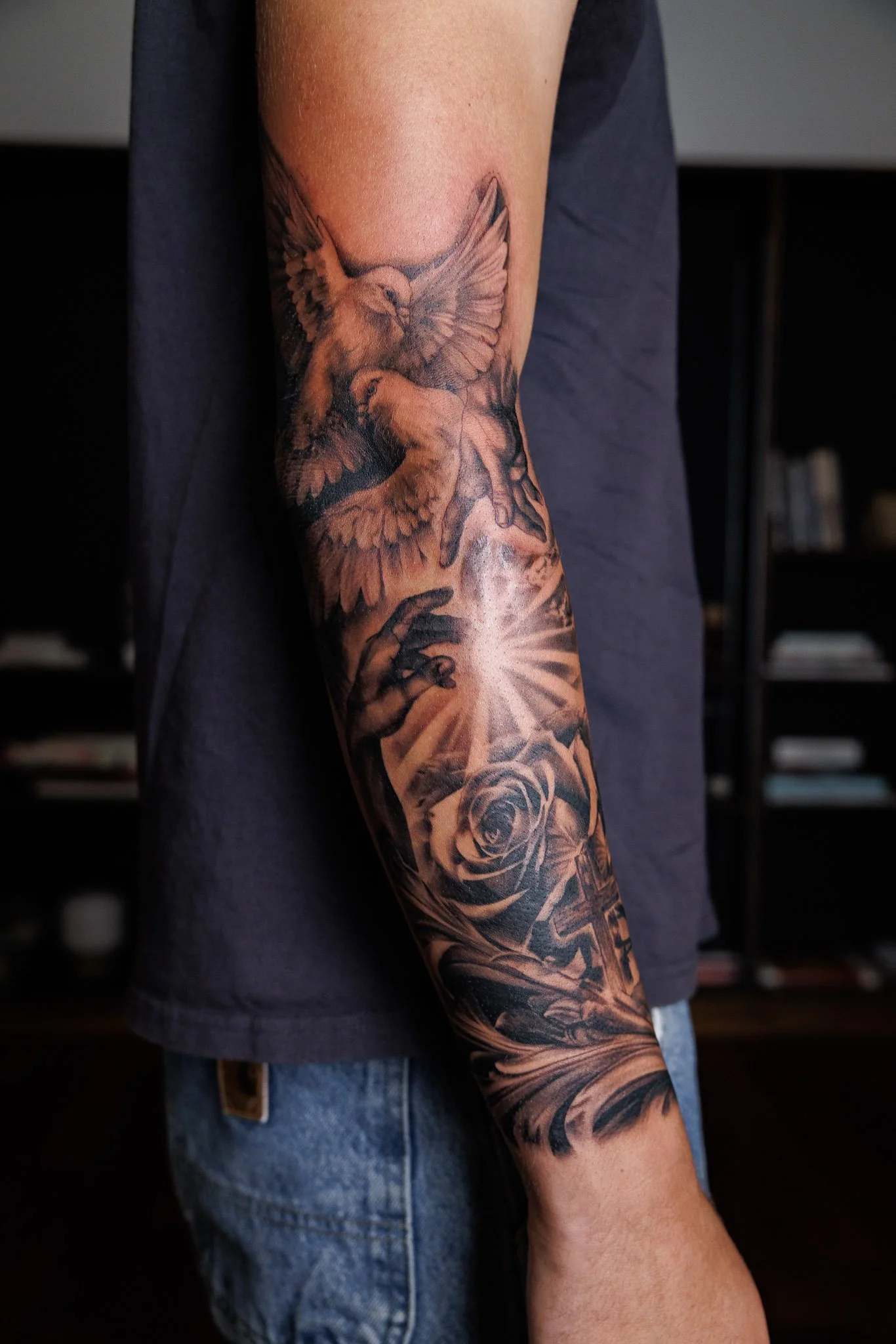 A person's arm with an intricate tattoo of a bird in flight, roses, and other floral elements.