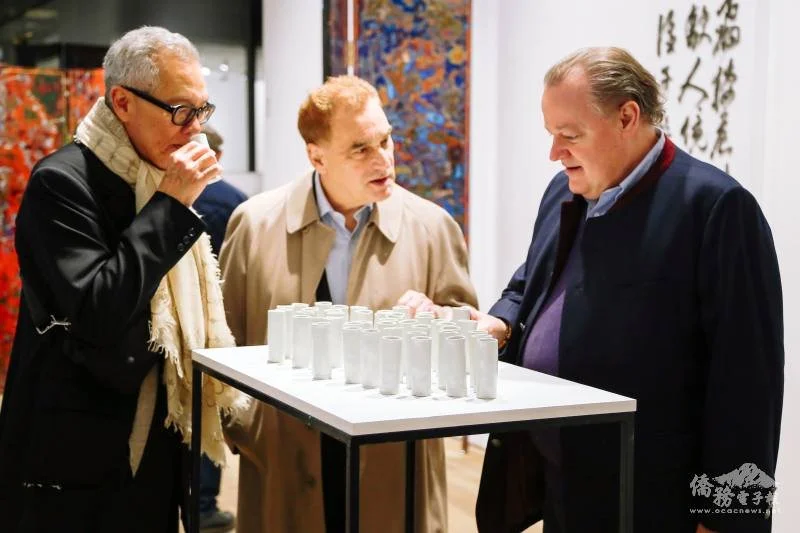 Trois personnes regardant une table avec plusieurs petits objets cylindriques dans une galerie d'art.