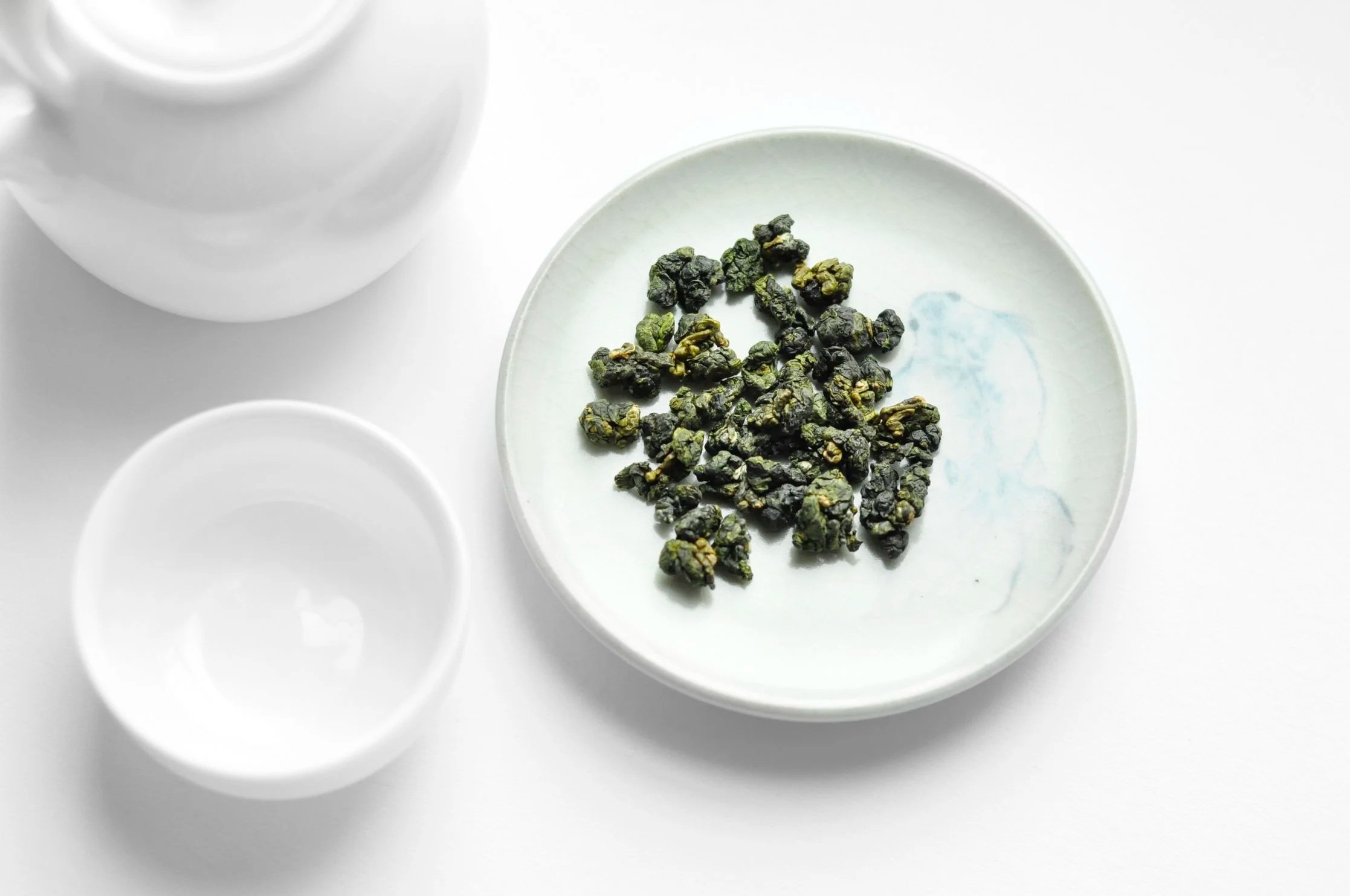 Tasses blanches et assiette blanche avec des grappes de thé en feuilles sèches.