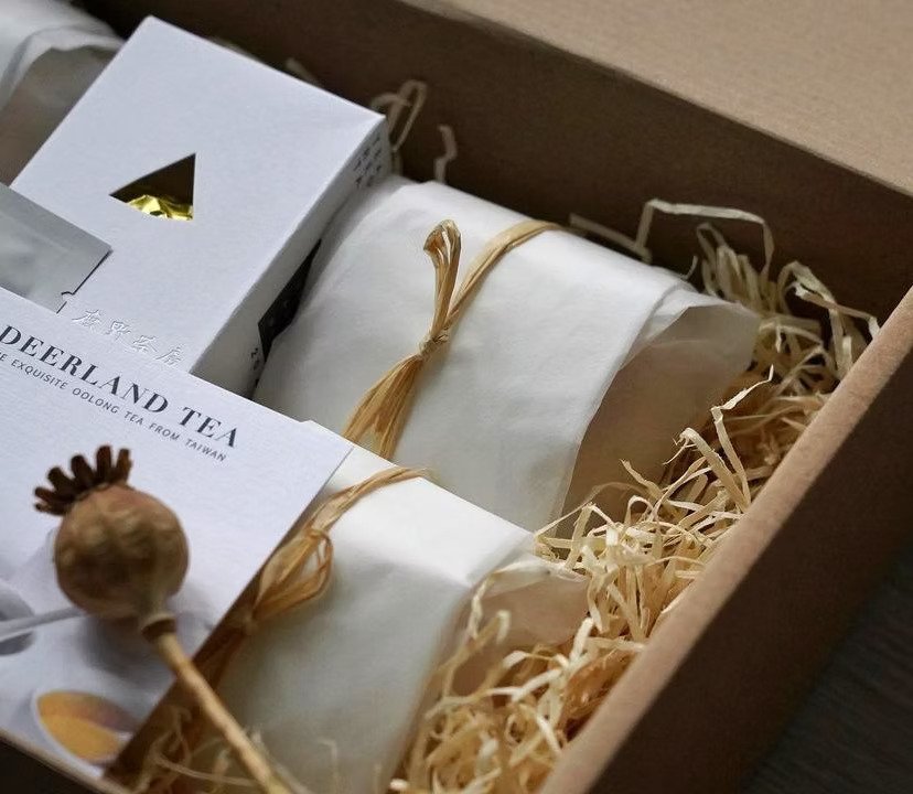 Boîte en carton contenant des produits de thé, des feuilles de papier, un paquet de thé blanc, et un moulin à herbes.