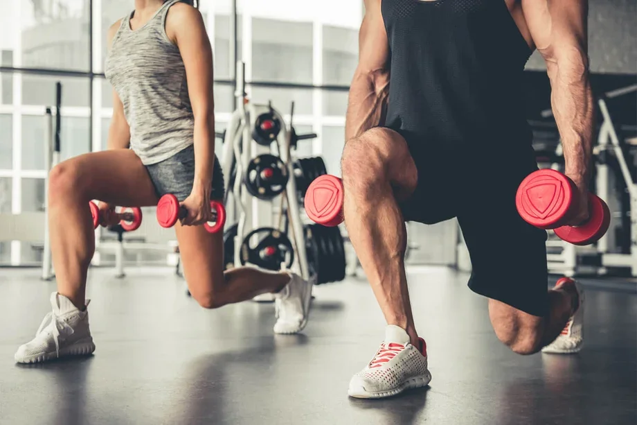 A man and woman holding dumbbells in low lunge position, getting ready to perform forward lunges during a Fit with Lisa workout.