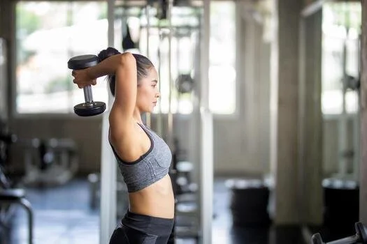 A woman performing a two-hand tricep extension with a dumbbell to target upper body strength during Fit with Lisa strength training