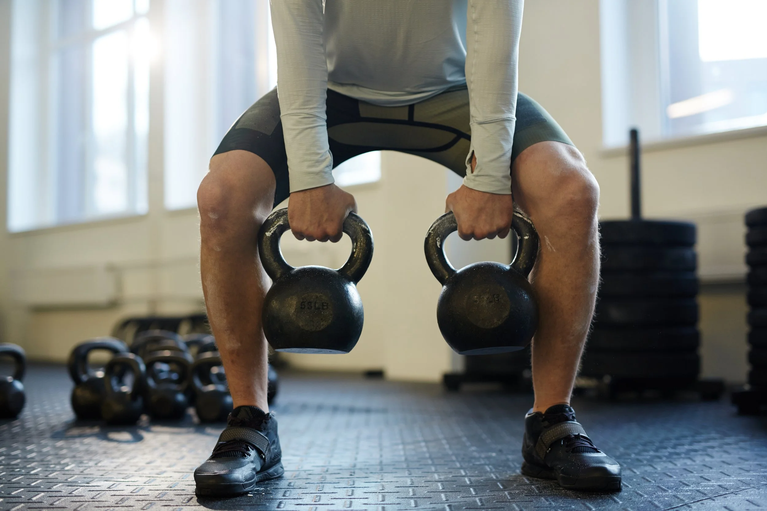 A man holding two kettlebells in a deep squat position during a strength training workout with Fit with Lisa.
