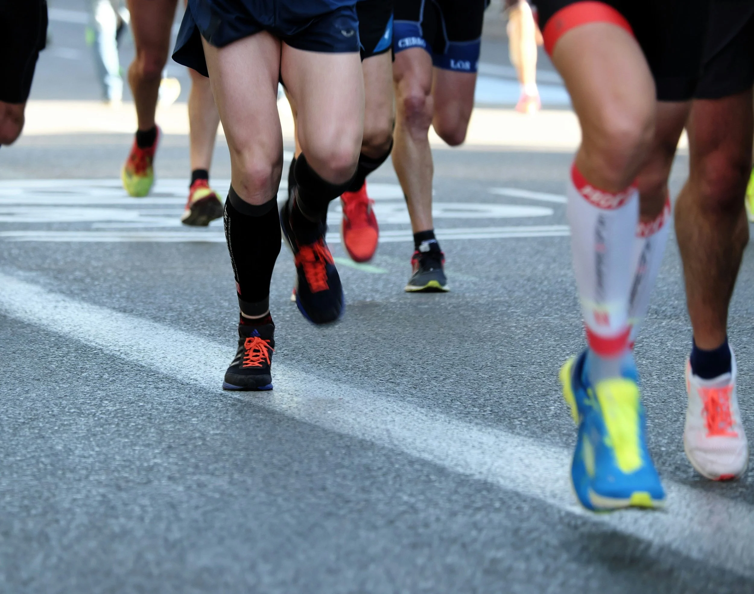 Close-up of runners' feet hitting the pavement during a race, symbolizing momentum for Fit with Lisa run coaching.