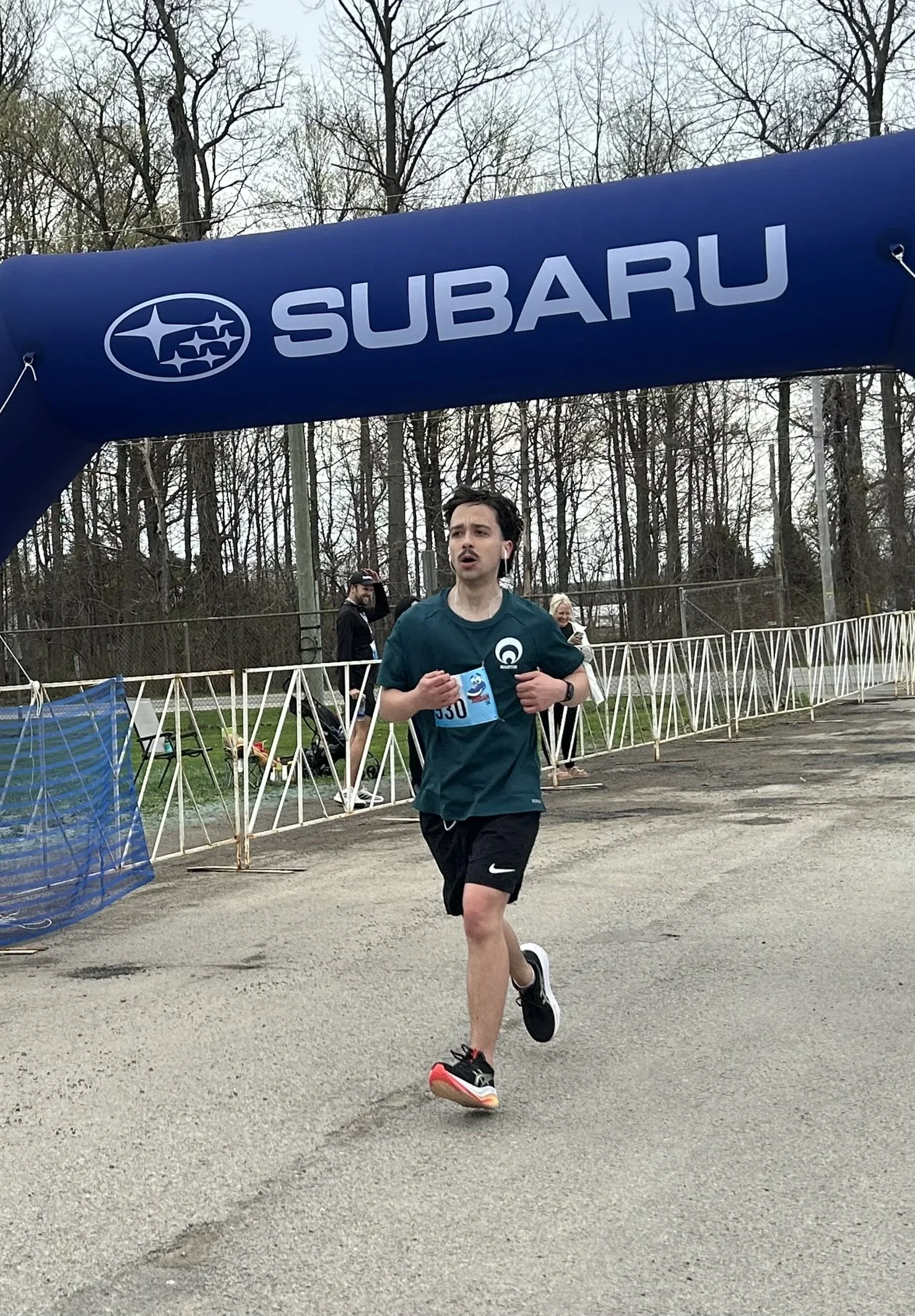 Martin crossing the Subaru finish line at a running race to achieve a personal best, wearing a Grimsby Run Collective shirt from Fit with Lisa coaching.
