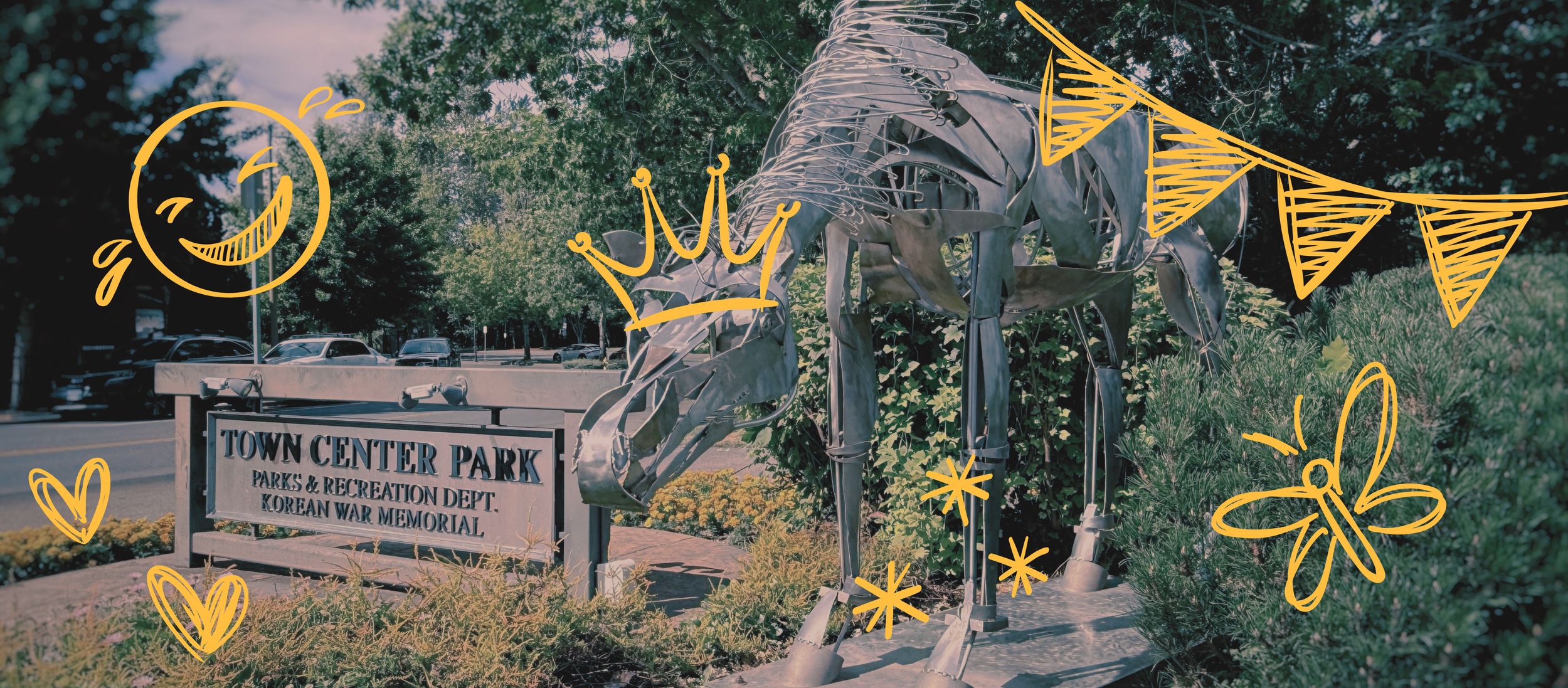 Metal sculpture of a horse, surrounded by yellow doodles of a smiley face, crown, hearts, stars, a butterfly, and bunting, in front of a park sign that reads 'Town Center Park.