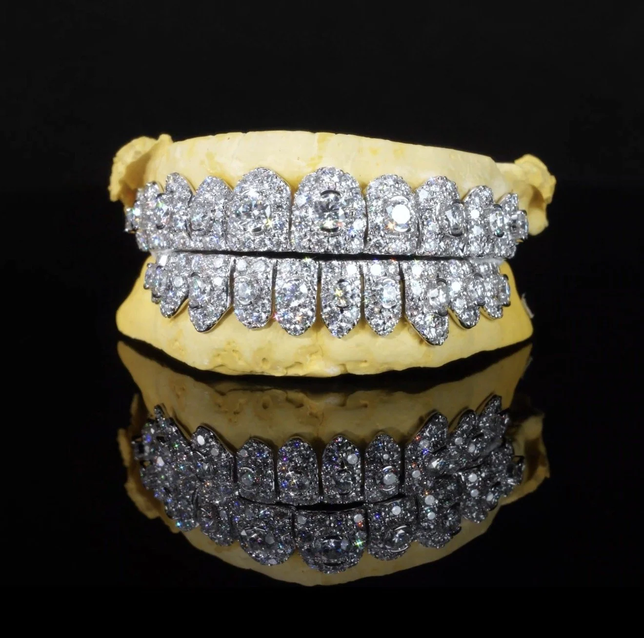A diamond-encrusted bracelet resting on a piece of yellow material, with its reflection visible on a glossy black surface.