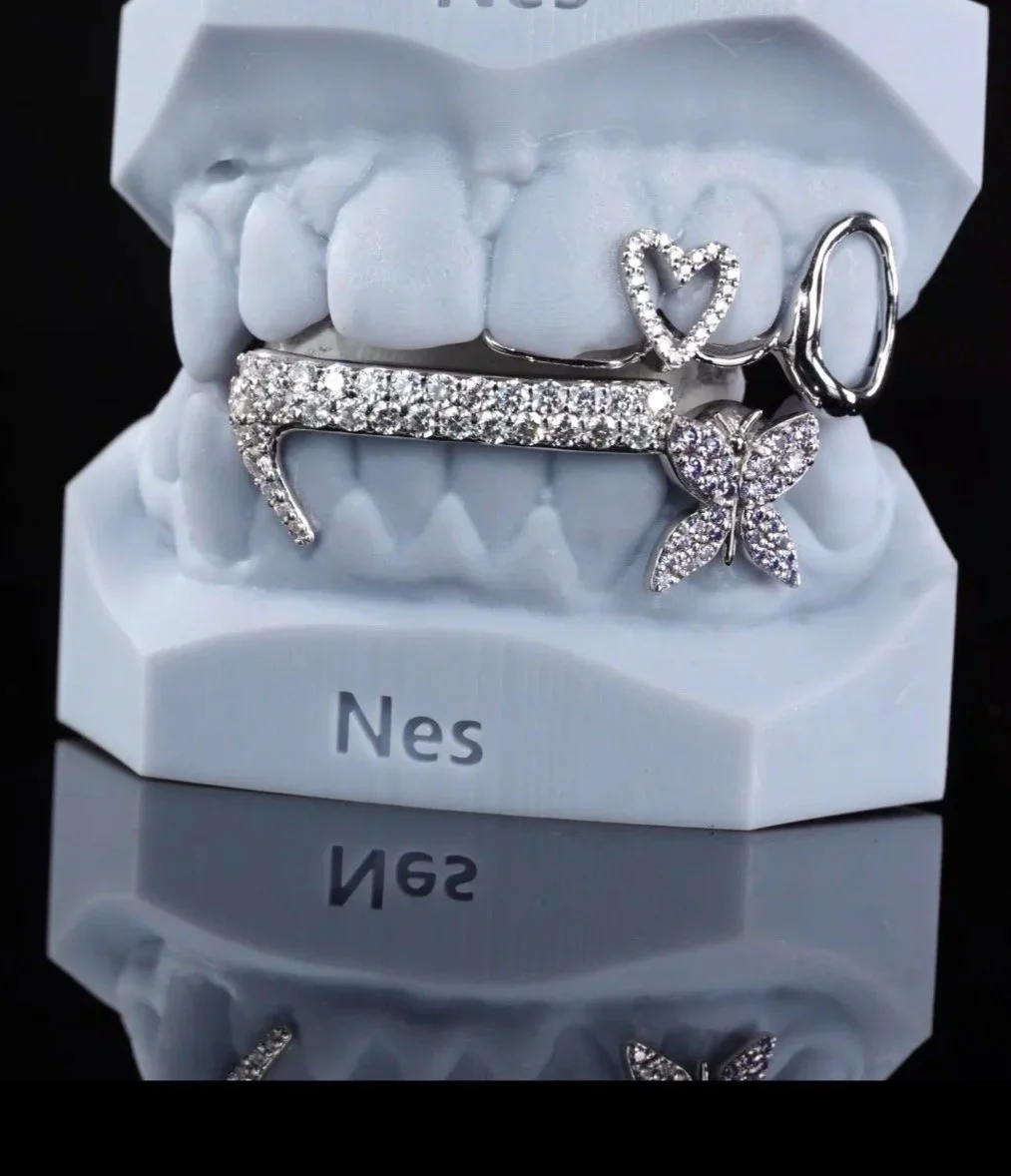 A white display model of teeth with jewelry attached, including a heart-shaped ring, a butterfly ring, and a body chain, with the brand name 'Nes' on the base.