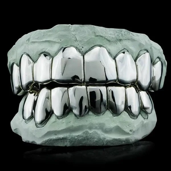 A dental mold with metallic dental grills on upper and lower teeth against a black background.
