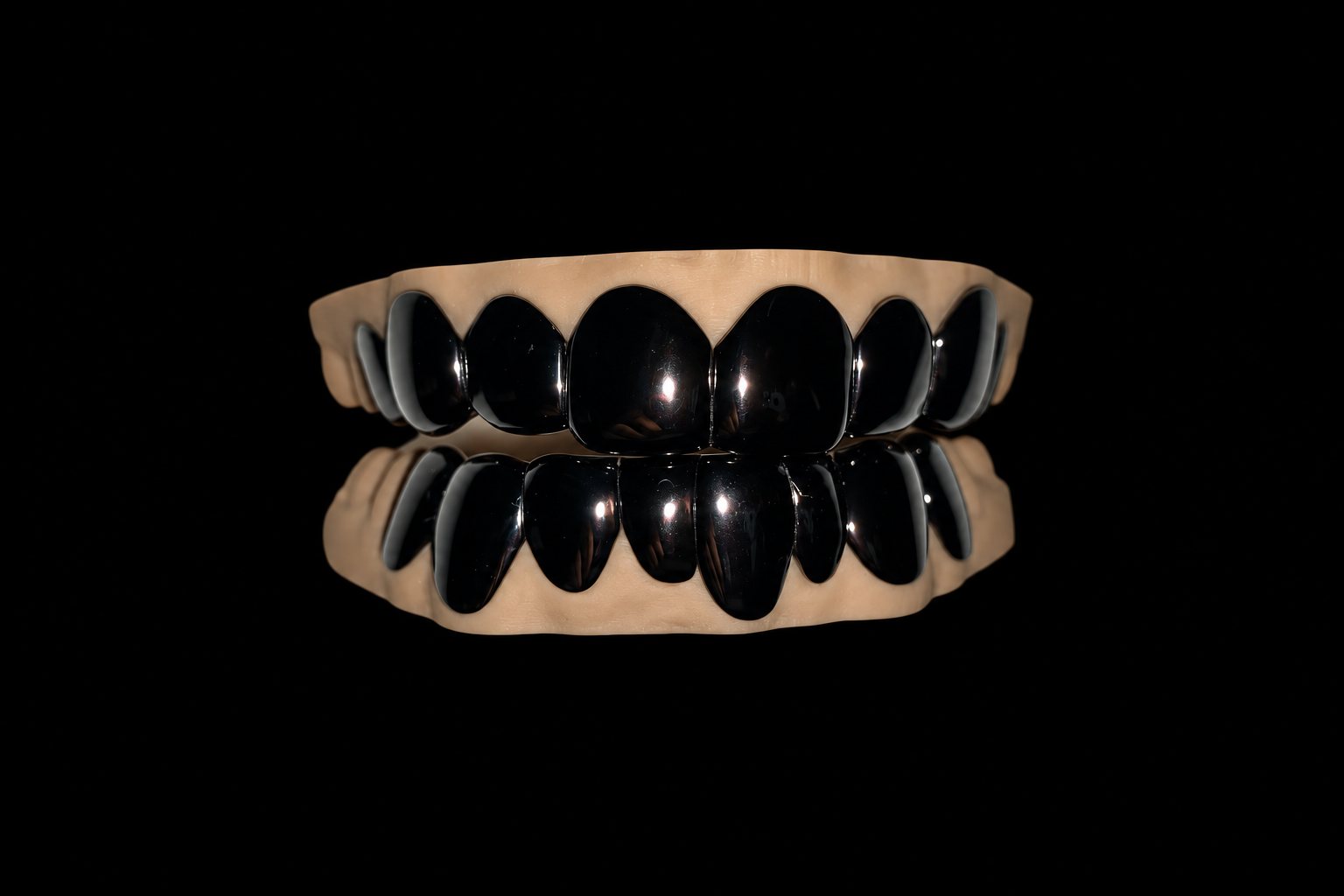 A set of shiny black and metallic teeth grills on a beige gum frame, with a reflection of the grills and gum on a black surface.