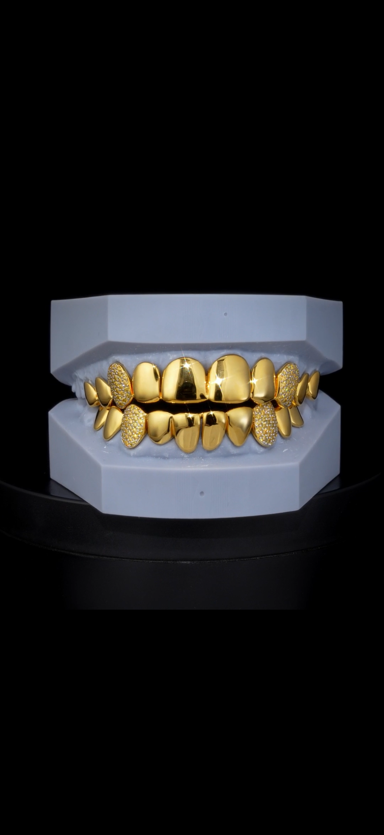 Gold grillz with diamond decorations on a white display case.