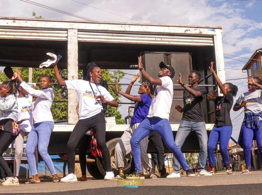 Group of people dancing and celebrating on a street in front of a truck with a speaker.