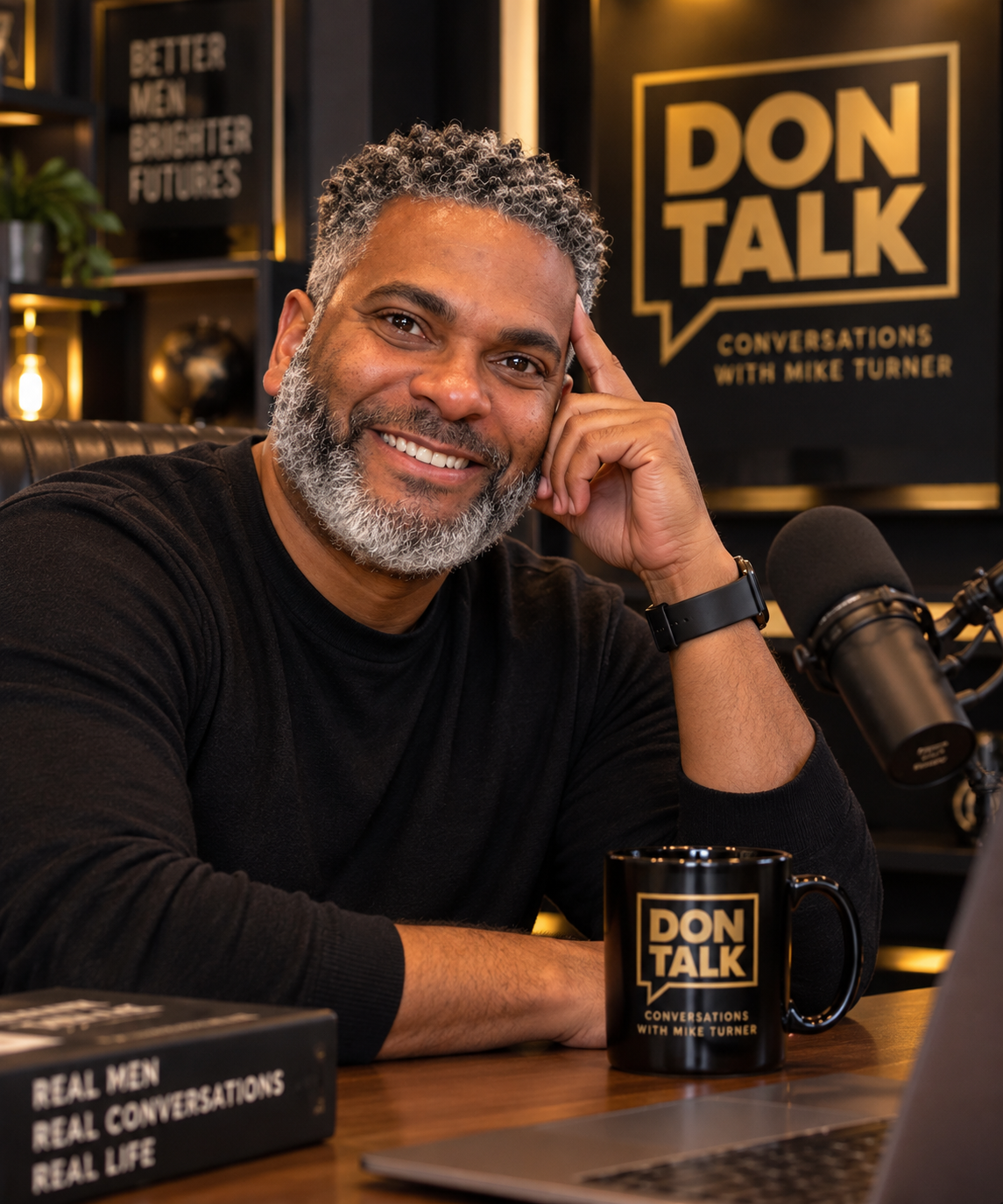 A middle-aged man with gray hair and a beard smiling at the camera, sitting at a table with a microphone and coffee mug, in a recording studio with the sign 'DON TALK Conversations with Mike Turner' in the background.