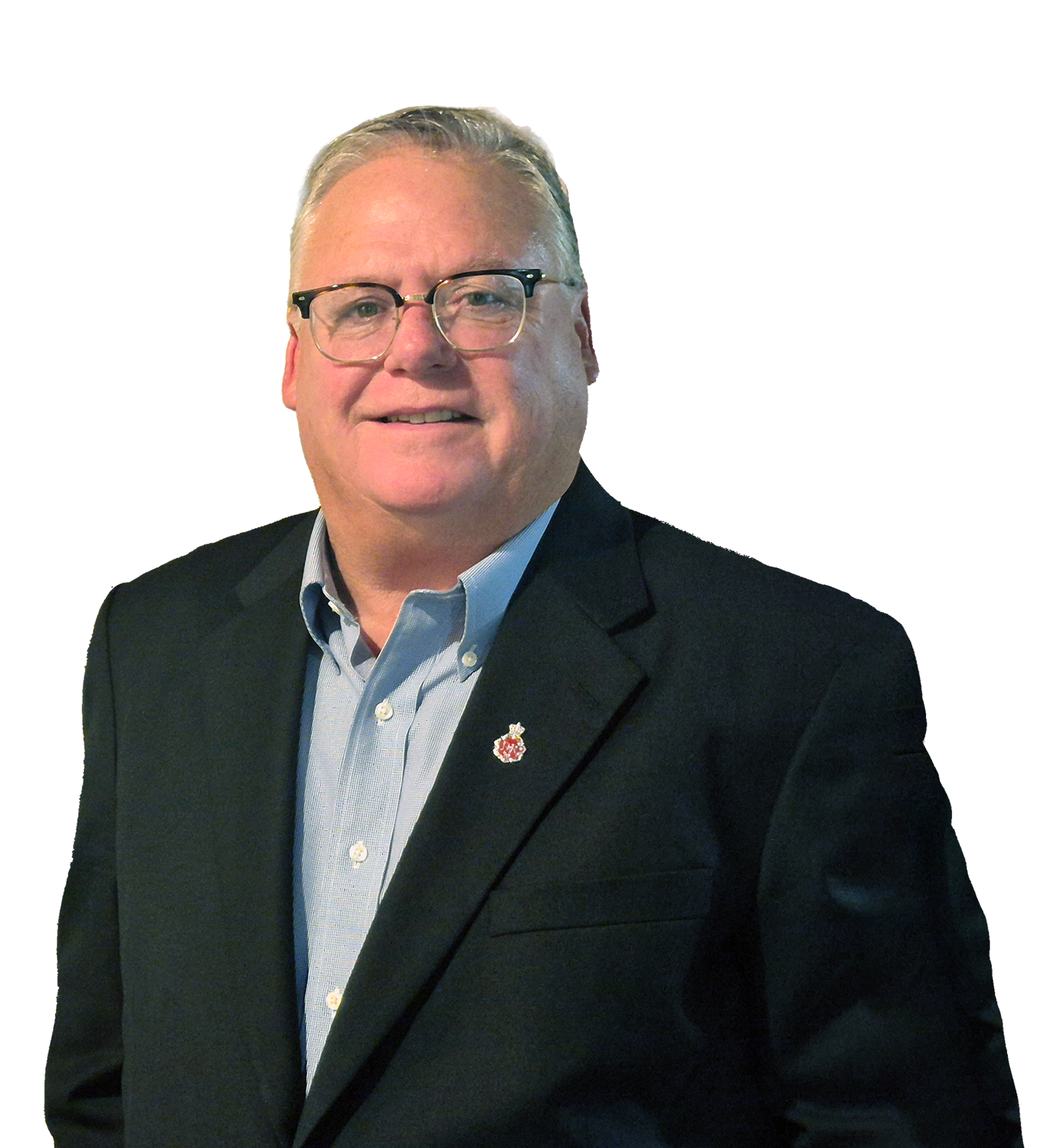 A man in a black suit with glasses and a white collared shirt, smiling, with a small red badge on his lapel.