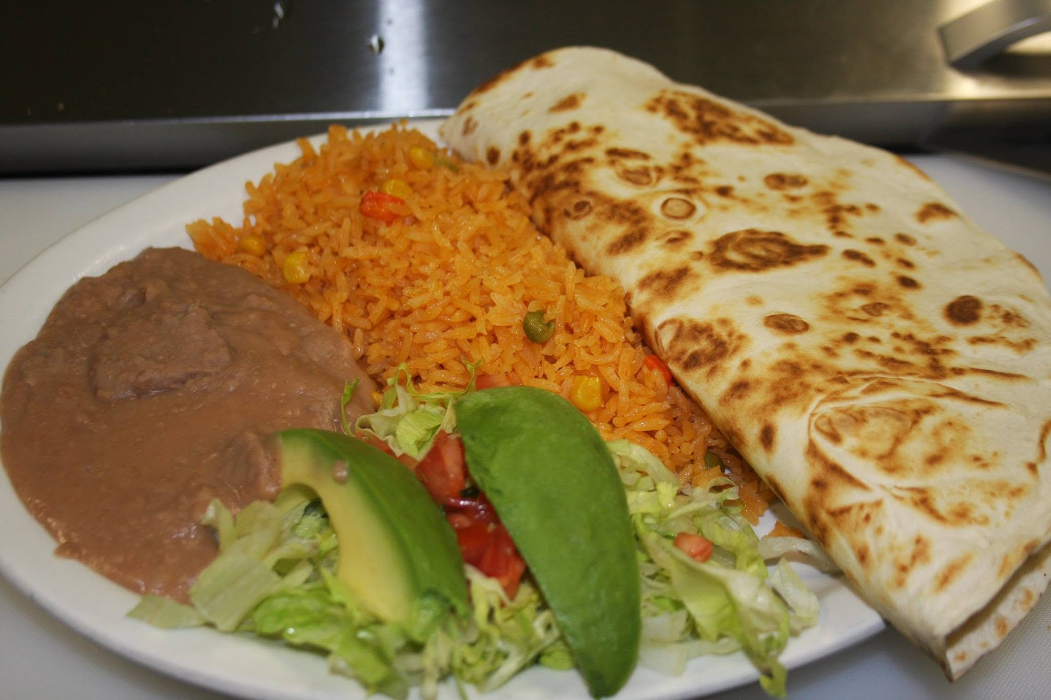 Plate of Mexican food including rice, a rolled taco, refried beans, and fresh salad with lettuce and tomato.