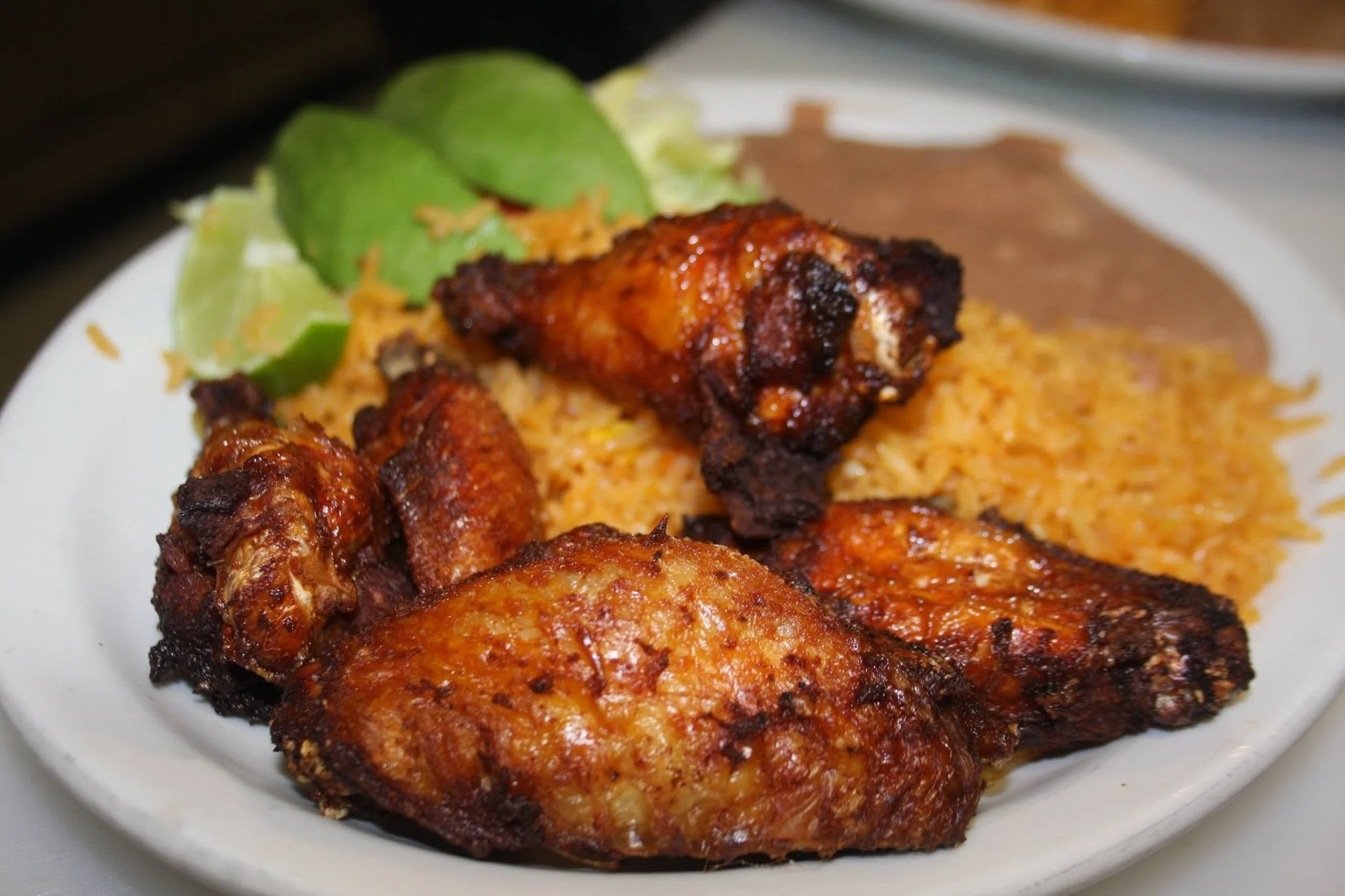 Close-up of grilled chicken pieces with a reddish-brown glaze, served with rice and lime wedges on a white plate.