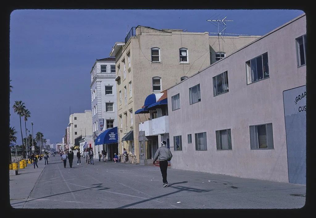 Ocean Front Walk in Venice in 1985, with storefronts and blue awnings along the Boardwalk