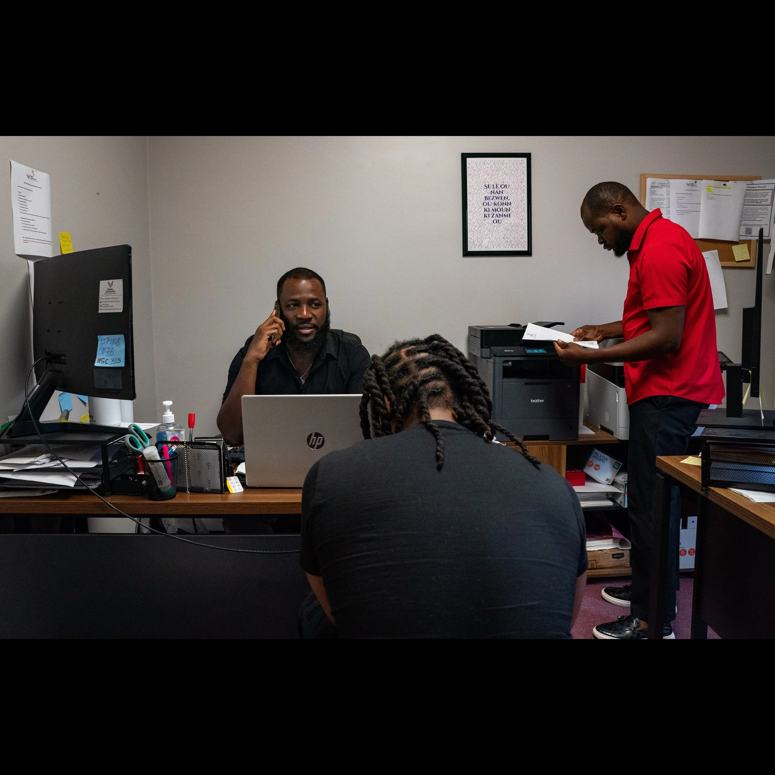 James Fleurijean, administrative assistant at the Haitian Community Help and Support Center in Springfield, helps a Haitian immigrant with paperwork before his mandatory immigration check later in the week as Viles Dorsainvil (right), co-founder and 