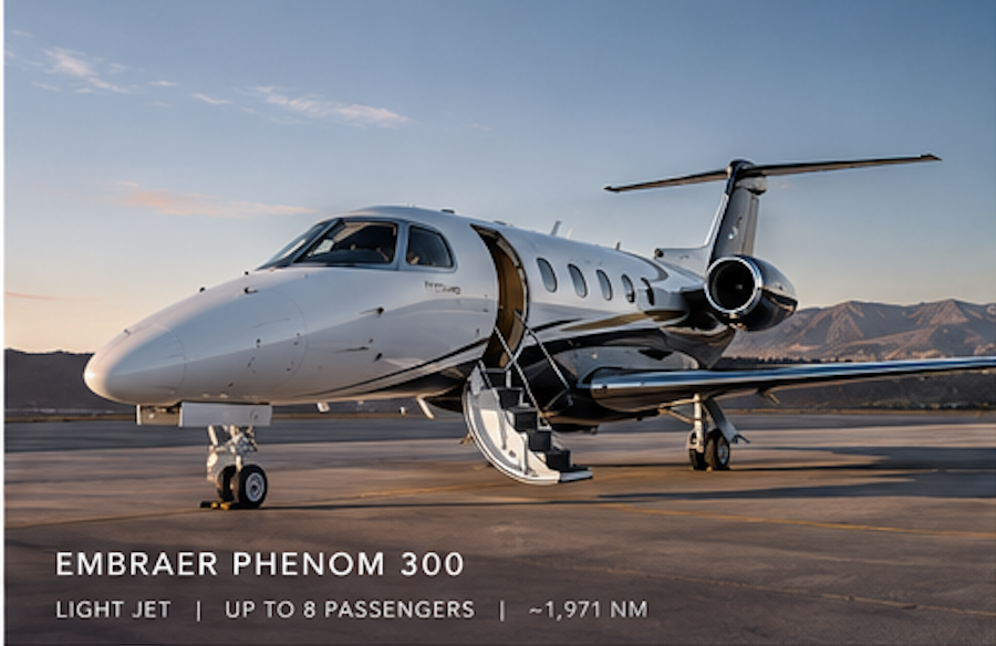 A white Embraer Phenom 300 private jet parked on an airport tarmac during sunset with mountains in the background.