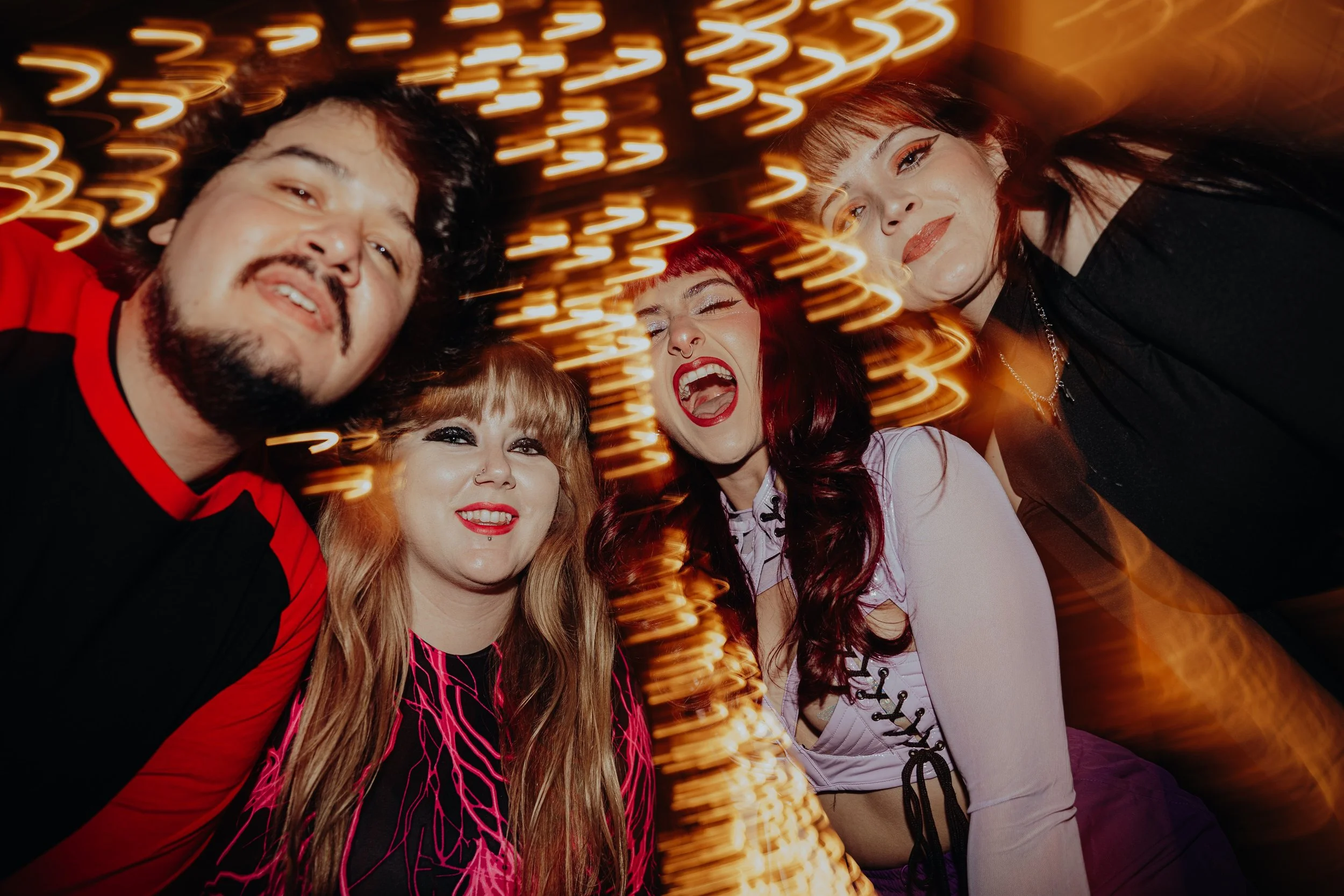 A group of five young adults smiling and having fun at a party, with colorful blurred lights in the background.