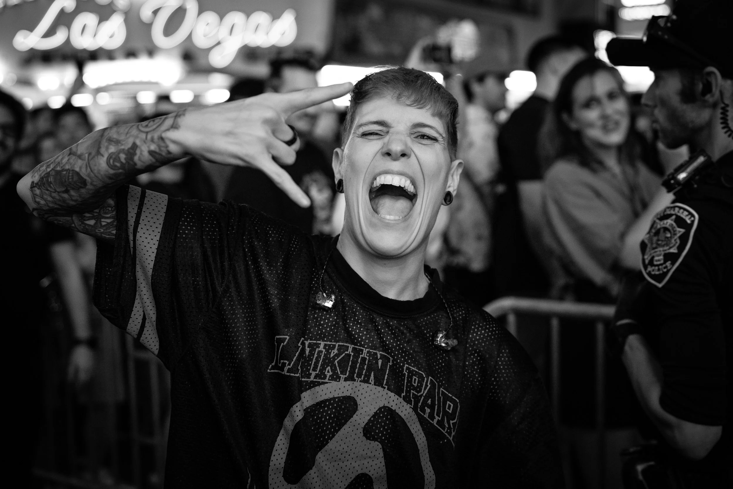 A woman with short hair and tattoos on her arm singing or yelling passionately at a crowded event, with several police officers in the background.
