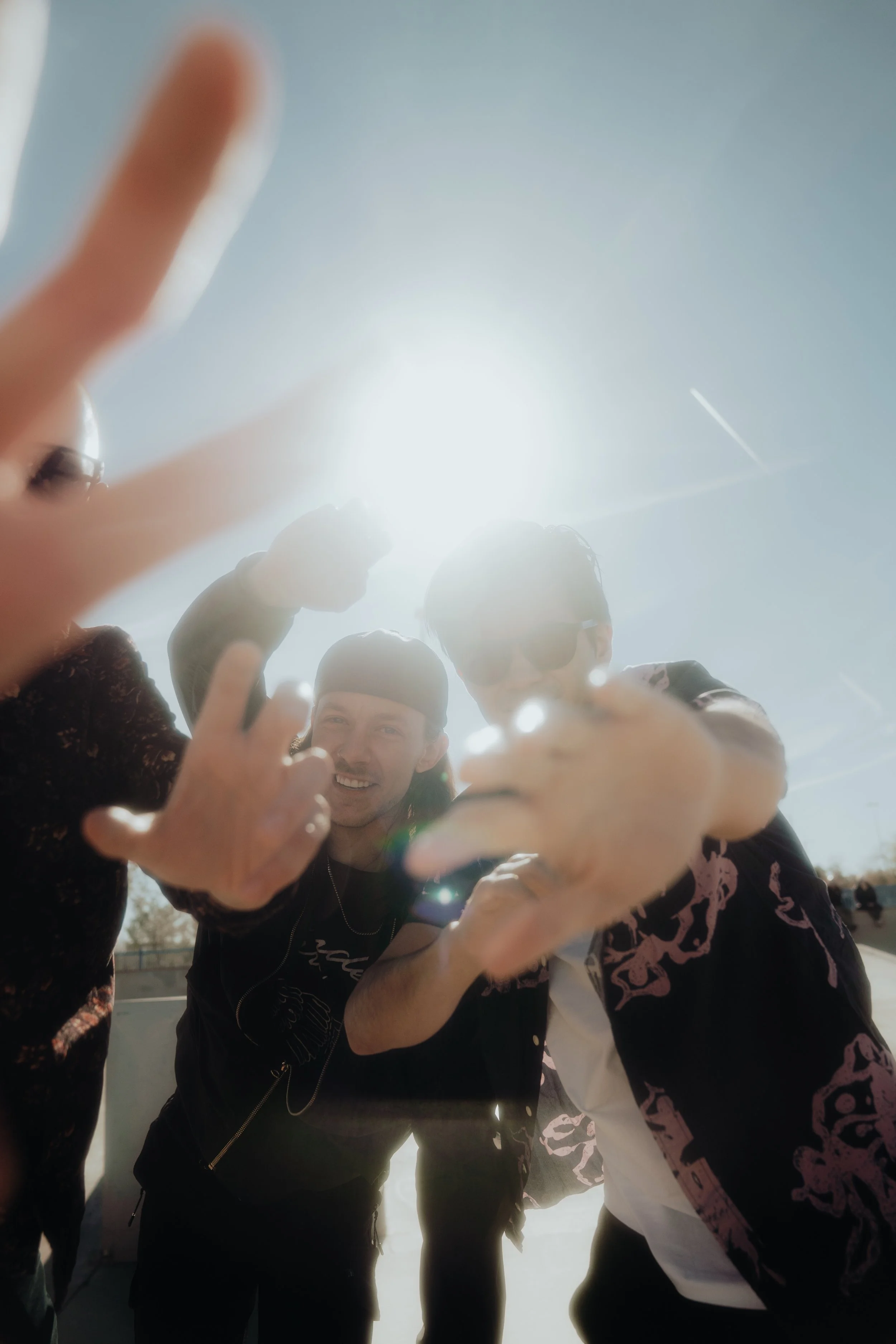 A group of people gathered outdoors, smiling and making peace signs towards the camera with the sun shining brightly behind them.