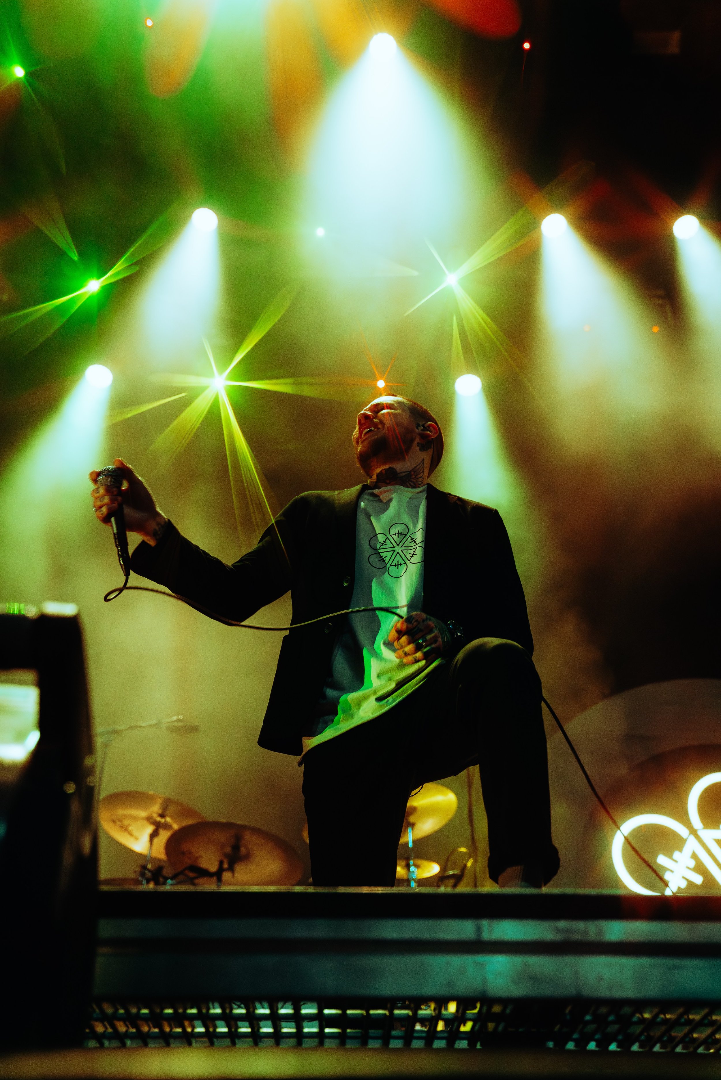 A male performer on stage holding a microphone, surrounded by colorful stage lights.