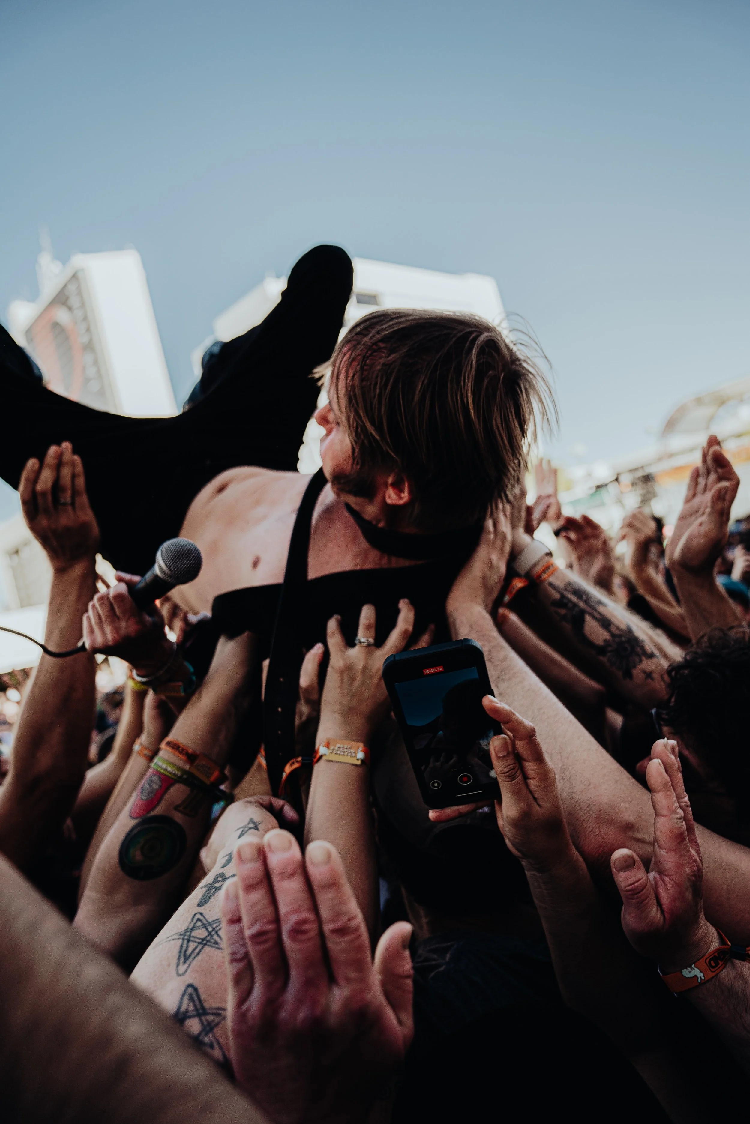 Crowd of concertgoers reaching toward a performer on stage, who is holding a microphone and appears to be singing, with people waving and embracing in the crowd.
