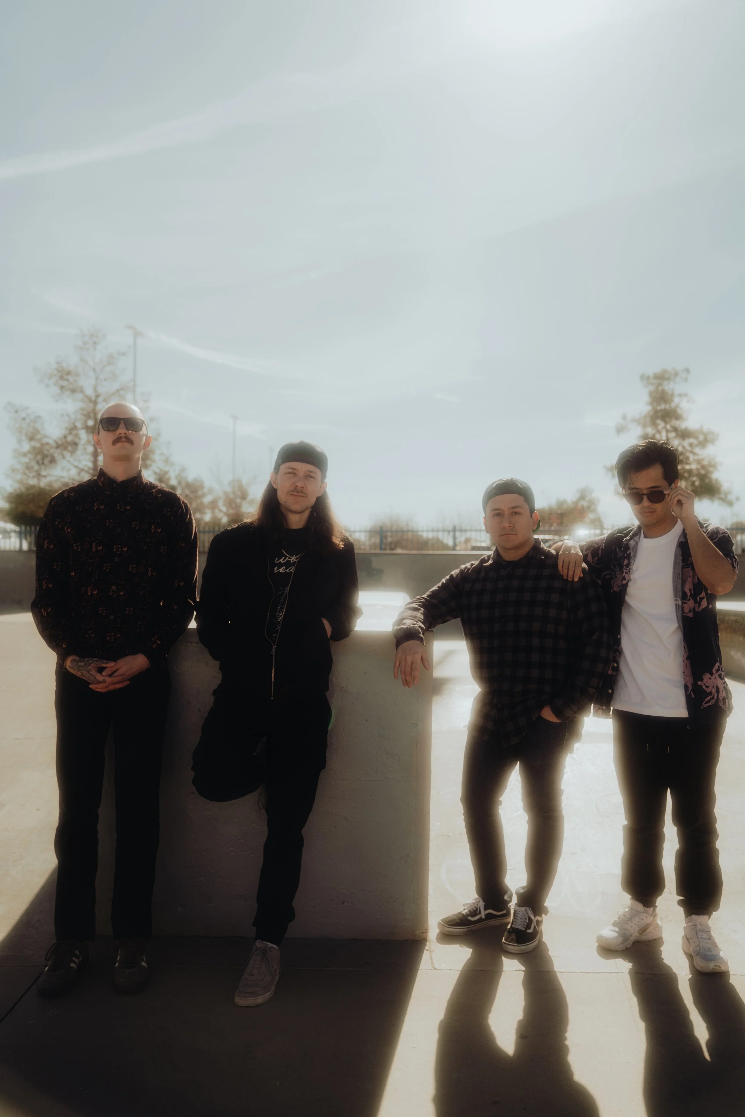 Four men standing outdoors, with the sunlight creating shadows on the ground behind them.