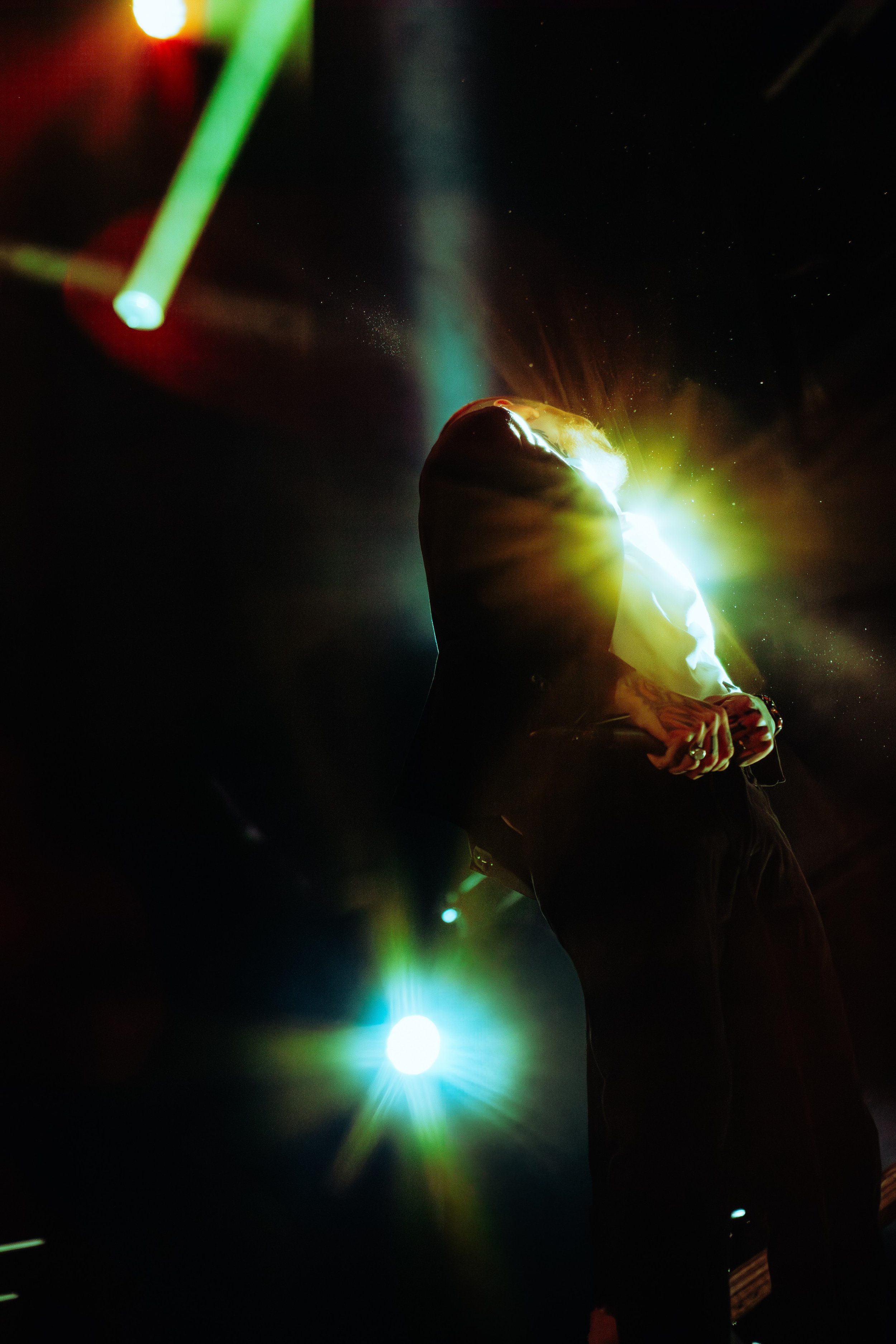 A person holding a bright light source in their hands, surrounded by colorful beams and lens flares in a dark environment.