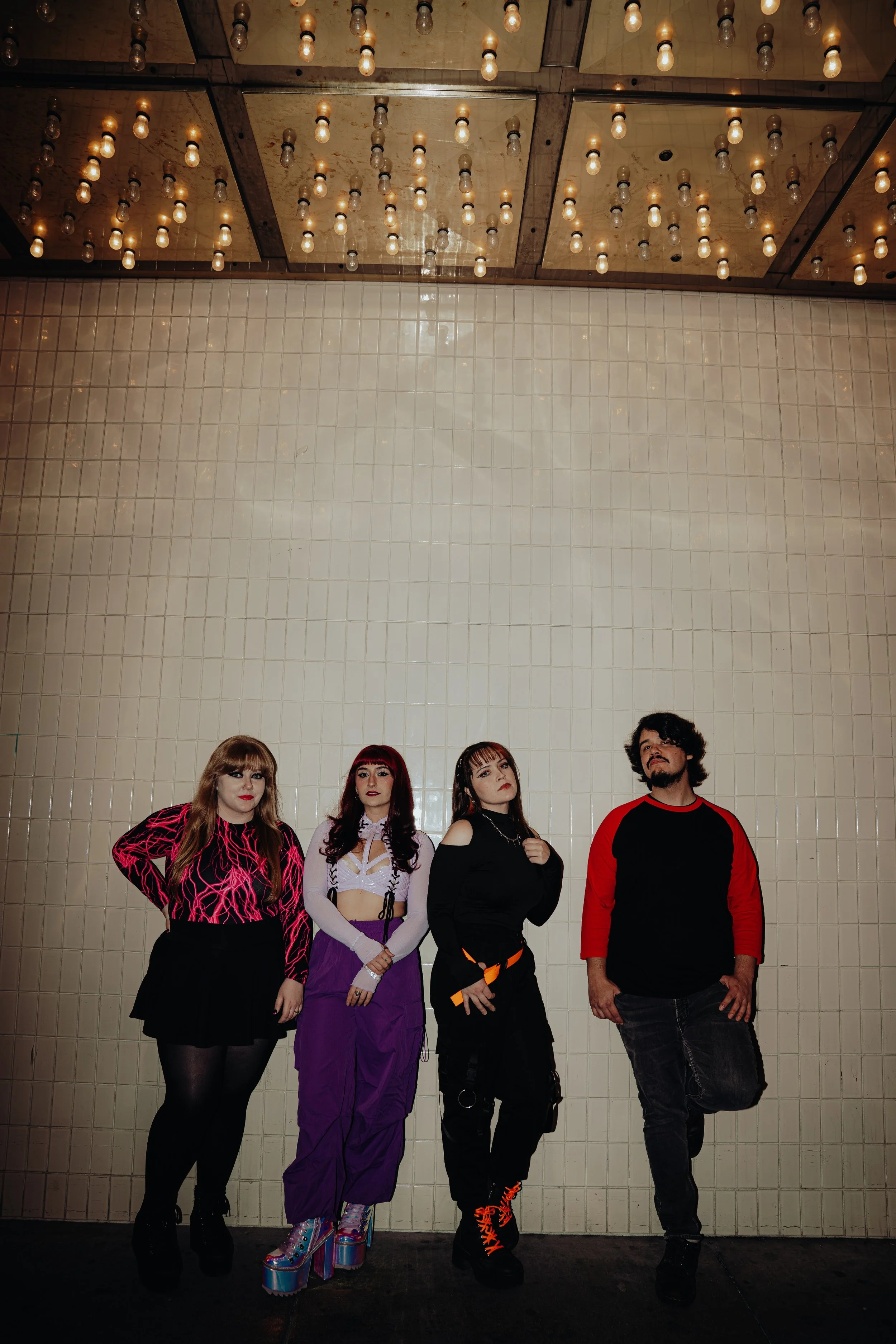 Five people standing in front of a beige tiled wall with a vintage light fixture on the ceiling.