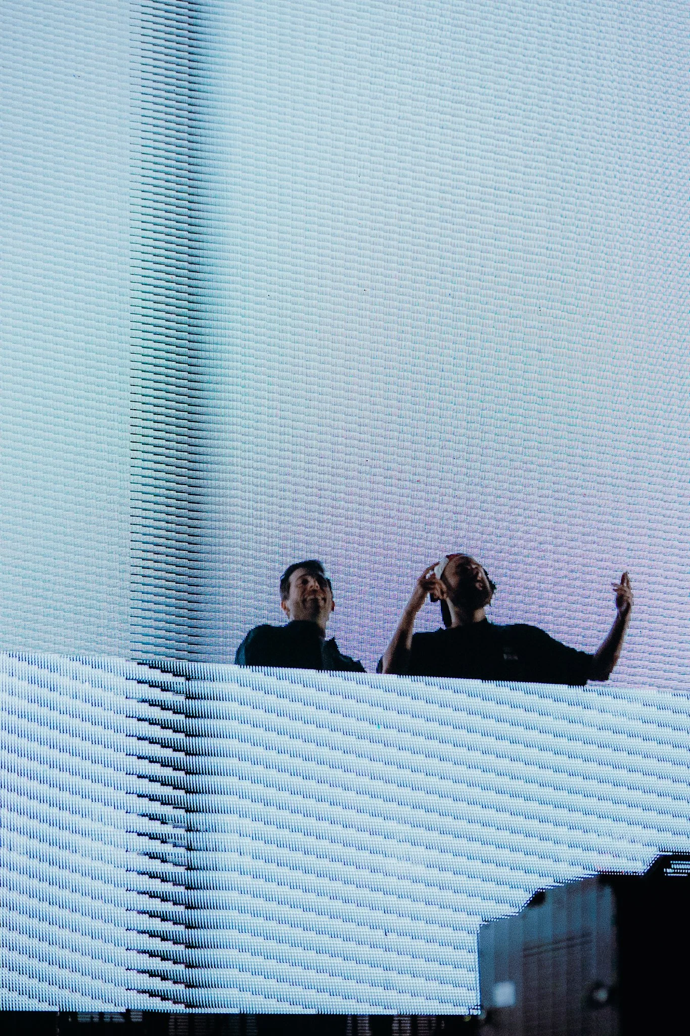 Two people standing in front of a large LED screen displaying an abstract pattern of lines and dots.
