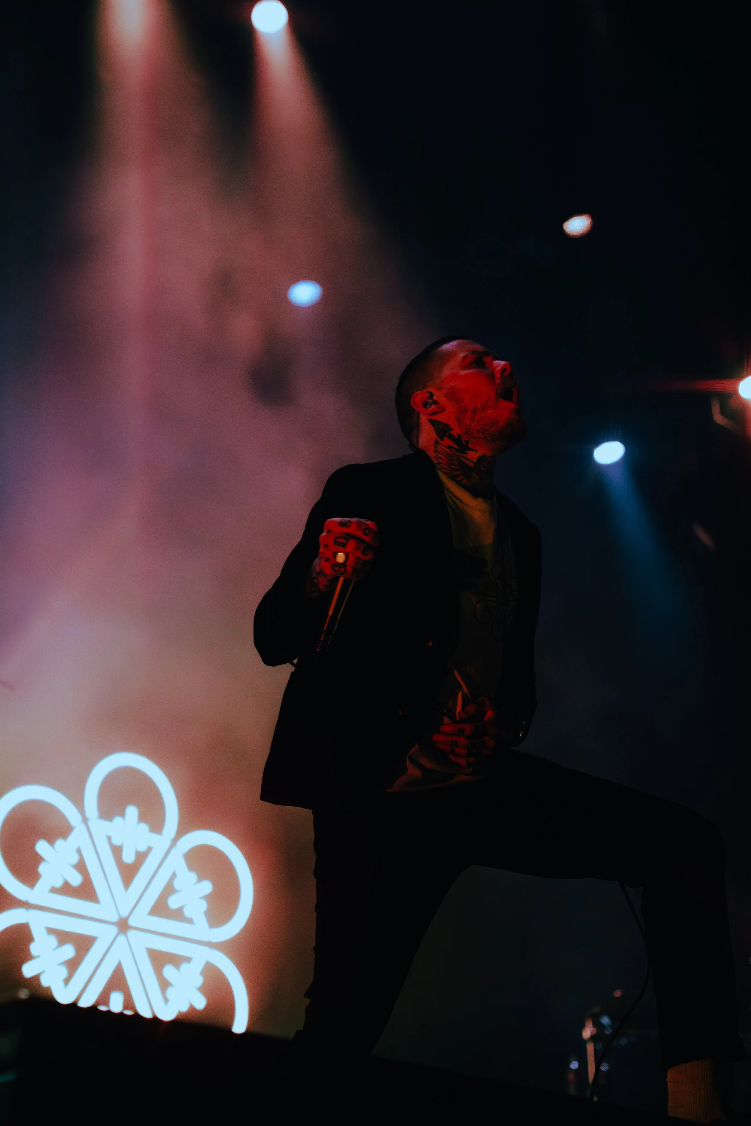 A man singing into a microphone on stage with colorful lights and a decorative snowflake design in the background.