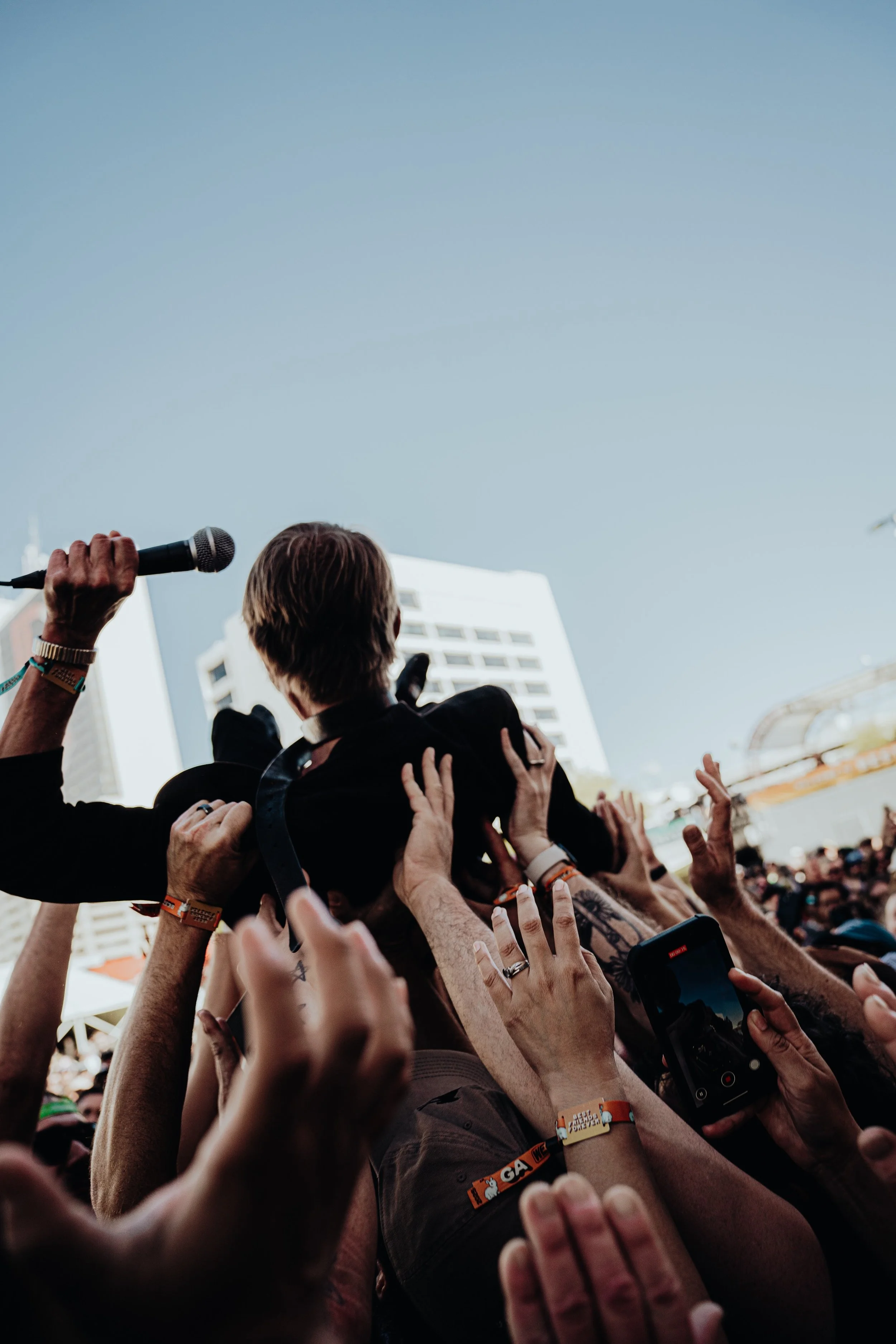 Crowd of people reaching out their hands towards a performer holding a microphone during an outdoor event in a city.