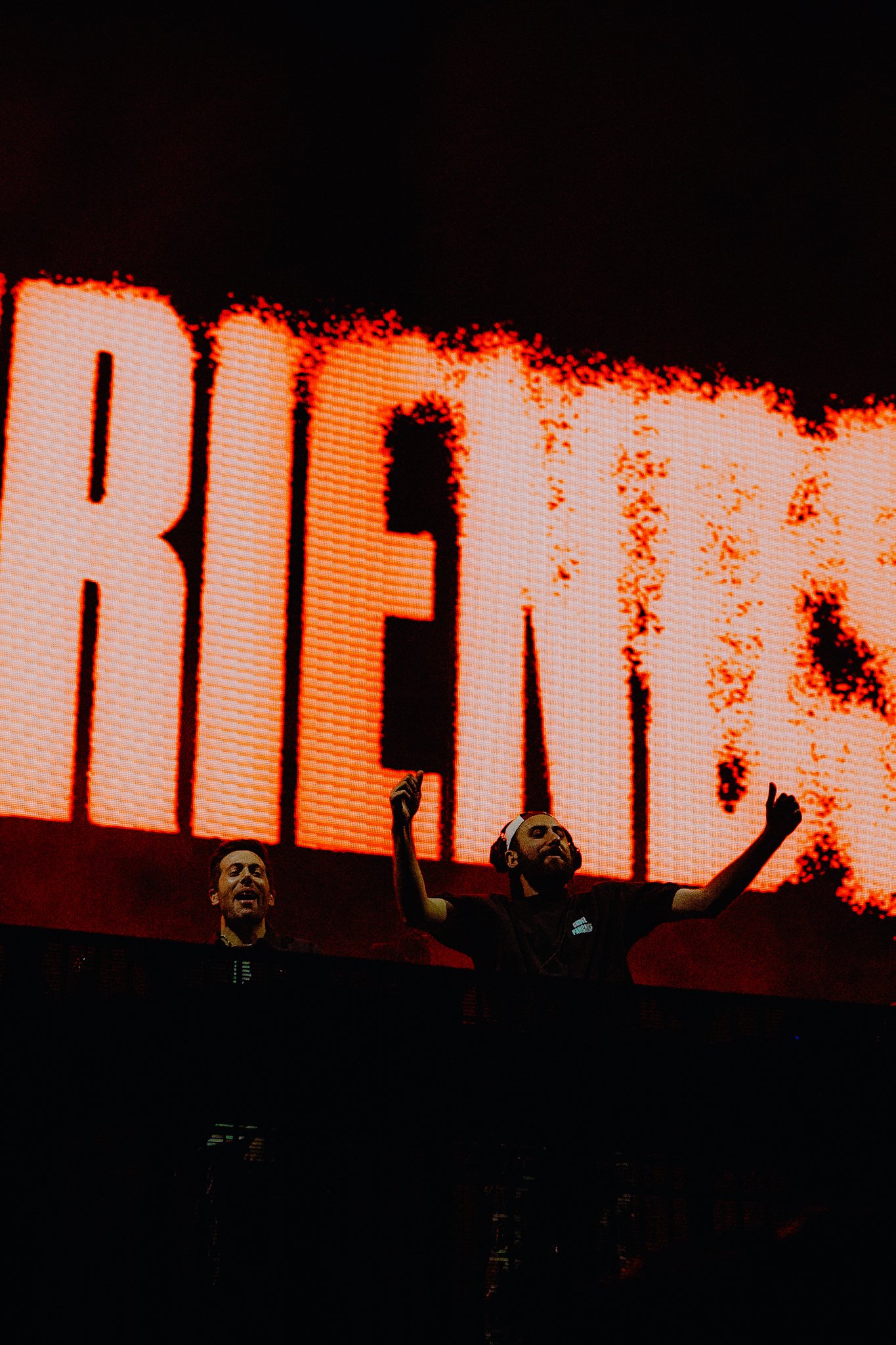 Two men are standing on a stage with one of them raising his arms. Behind them is a large, illuminated digital screen displaying the word "END" in red.