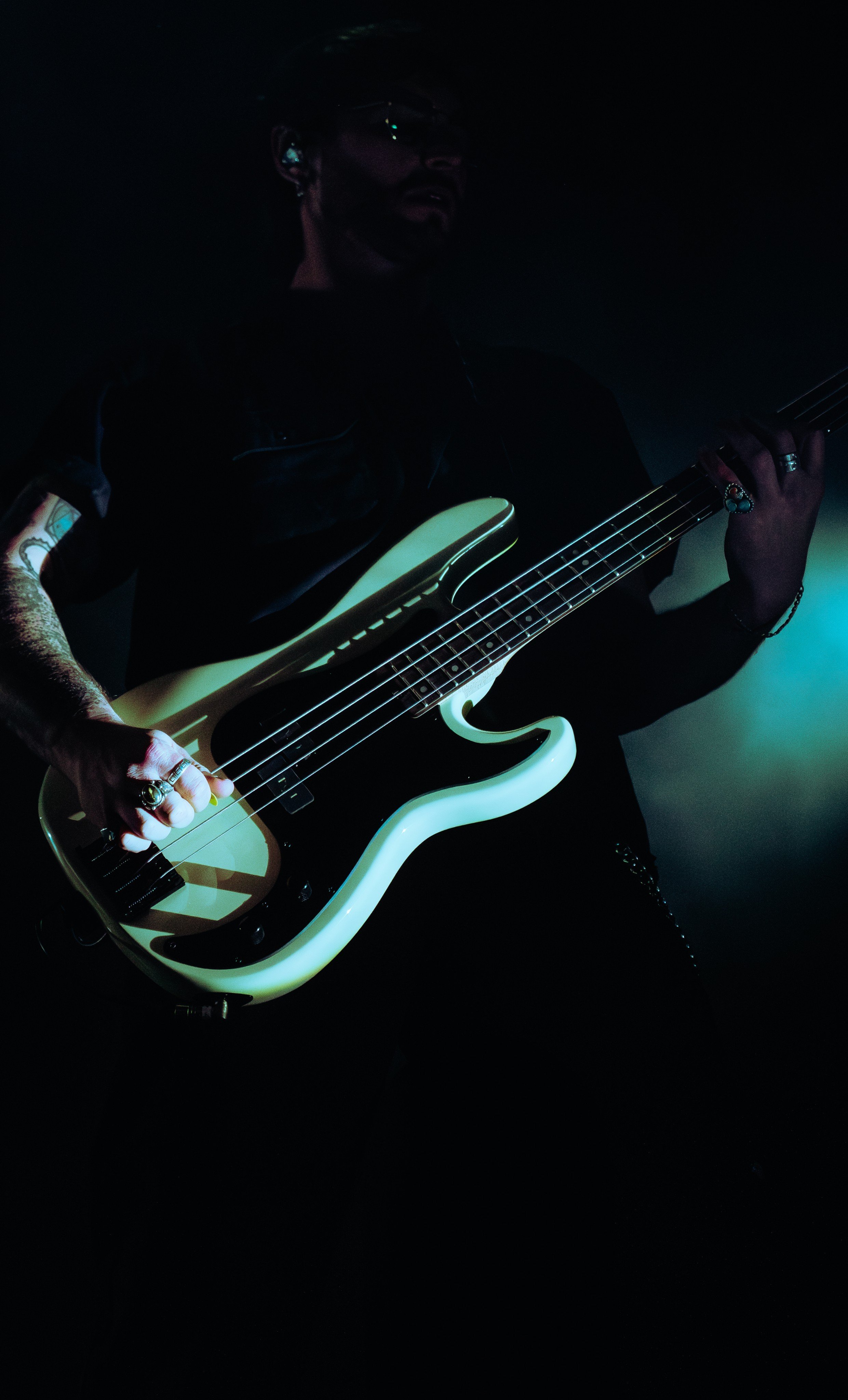 A man playing an electric bass guitar in a dark setting, illuminated with minimal lighting