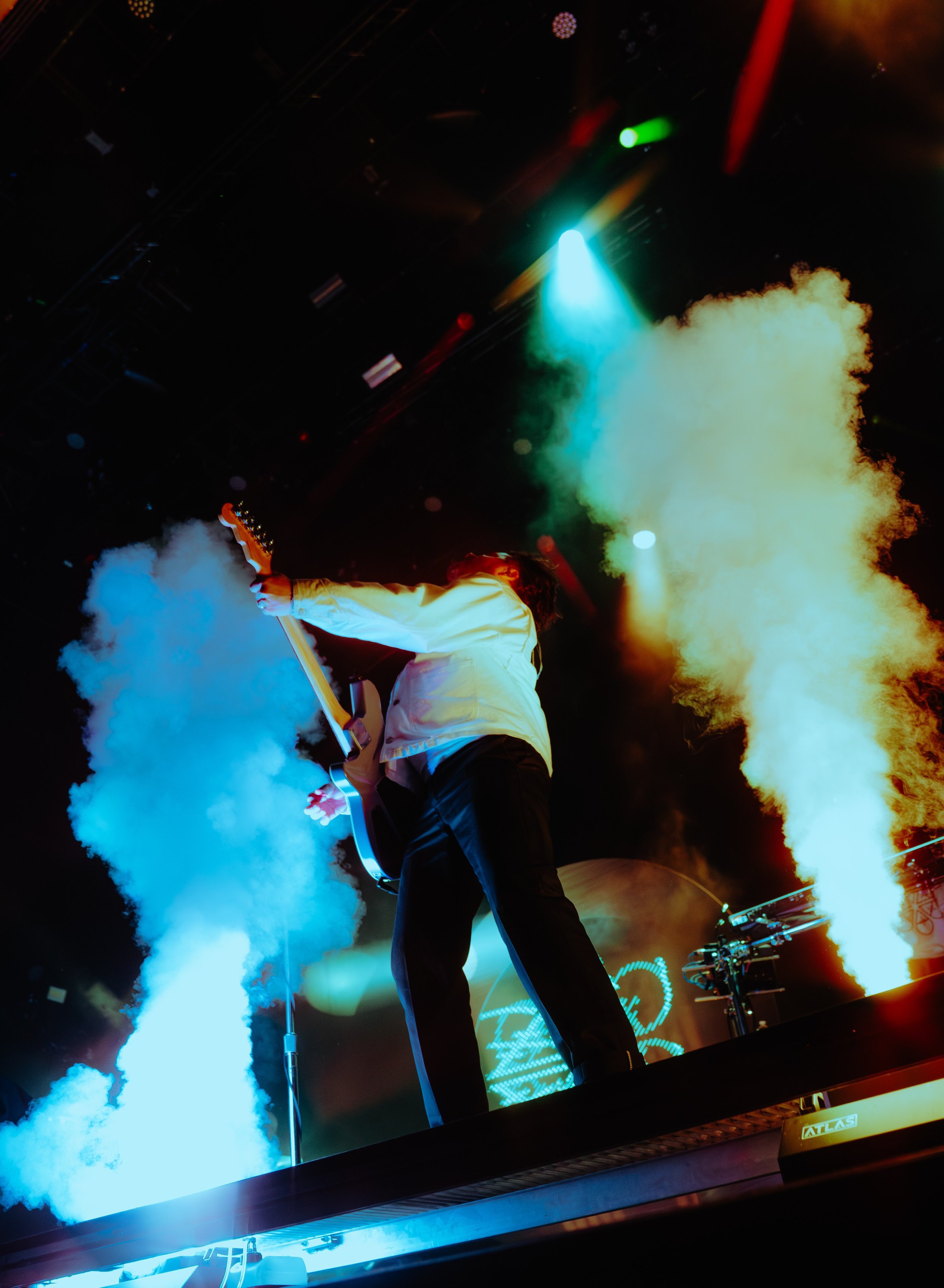 Musician playing guitar on a stage with colorful lights and smoke effects.