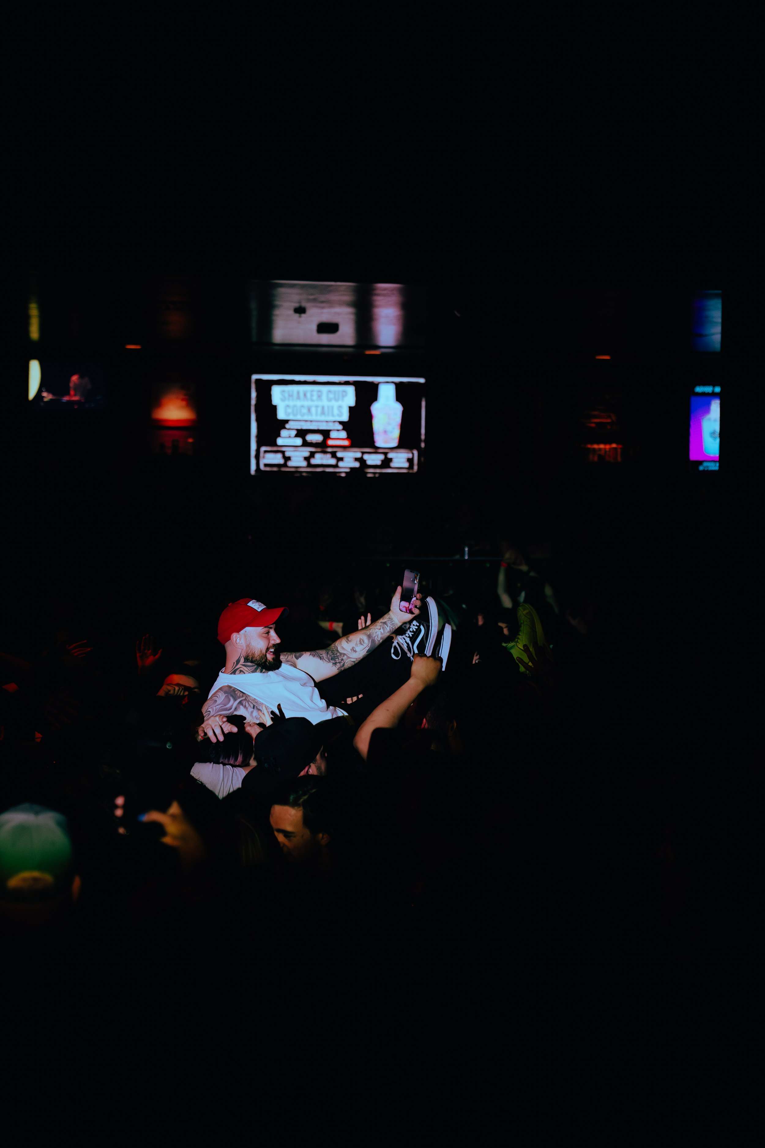 Crowd of people at concert or event, with a performer or speaker on stage in the background, illuminated by screens displaying text and images.