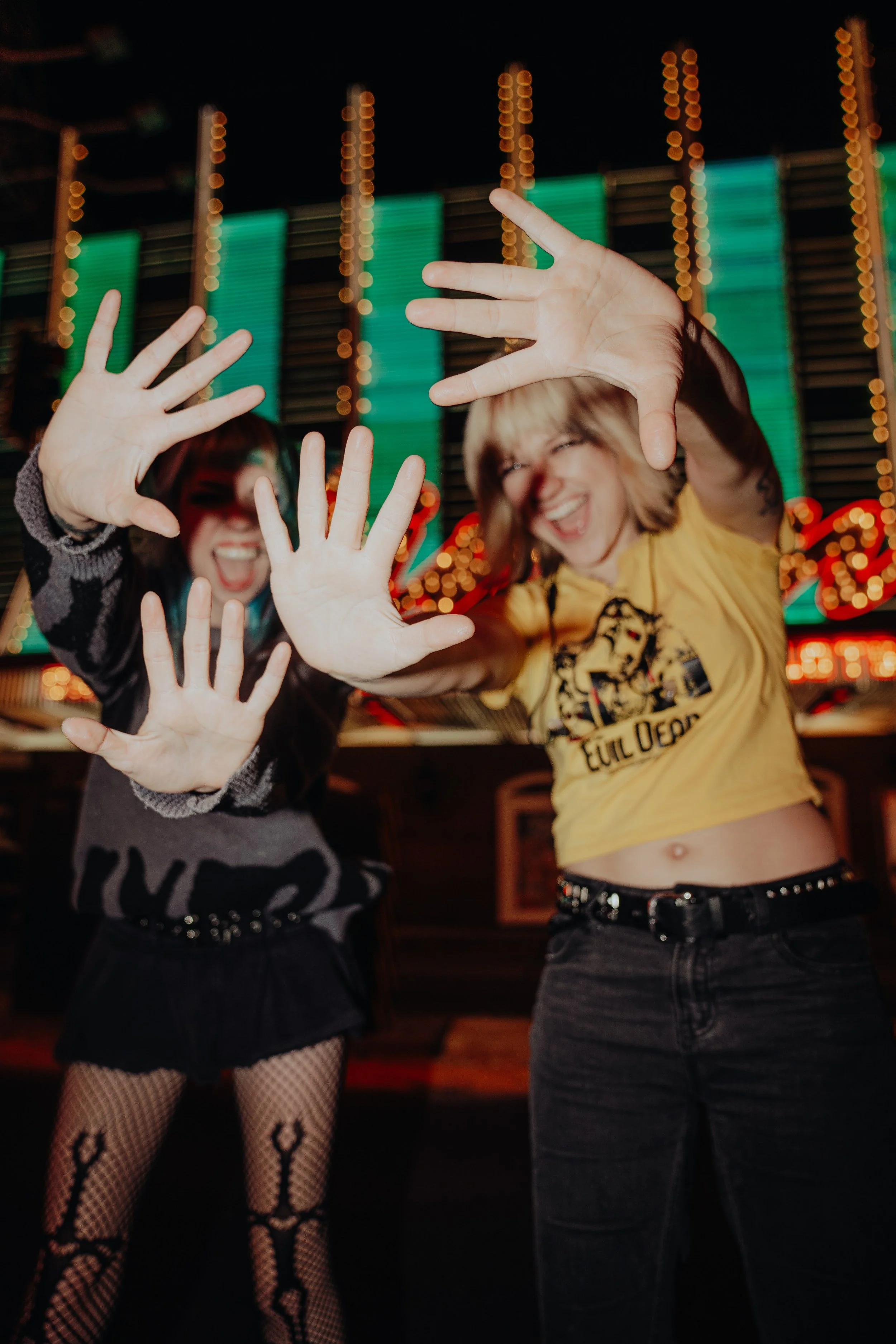 Two women dancing in a dimly lit room with colorful lights, showing their hands raised and smiling faces.