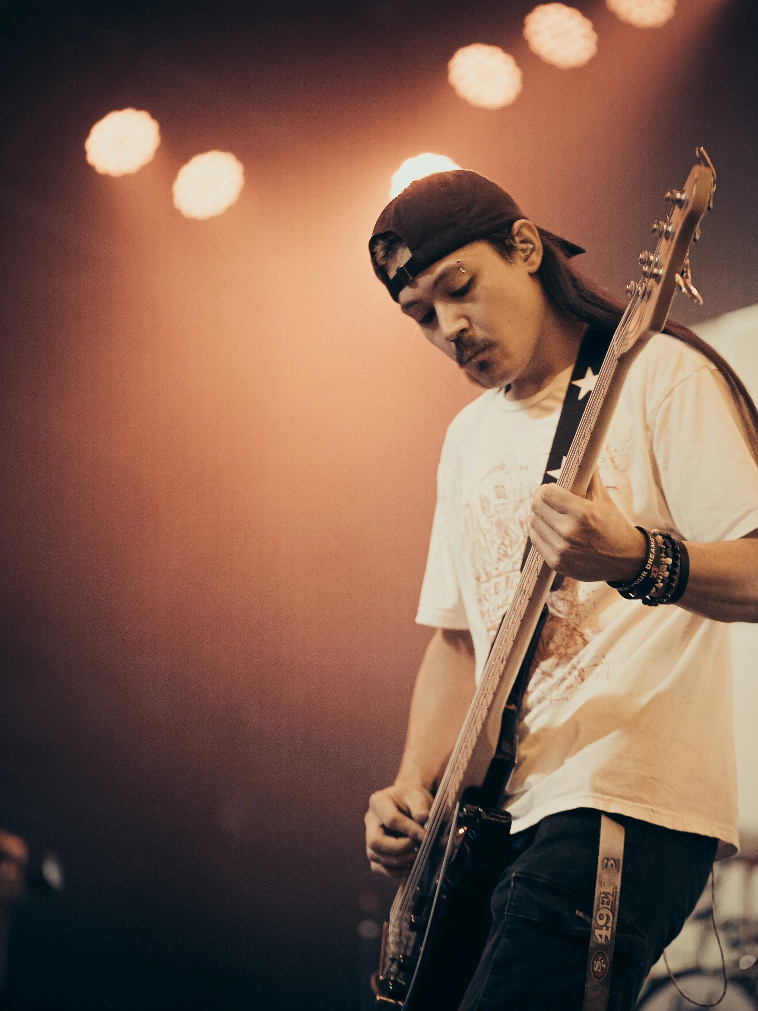 A person wearing a black cap playing an electric guitar on stage, with a blurred background of stage lights.