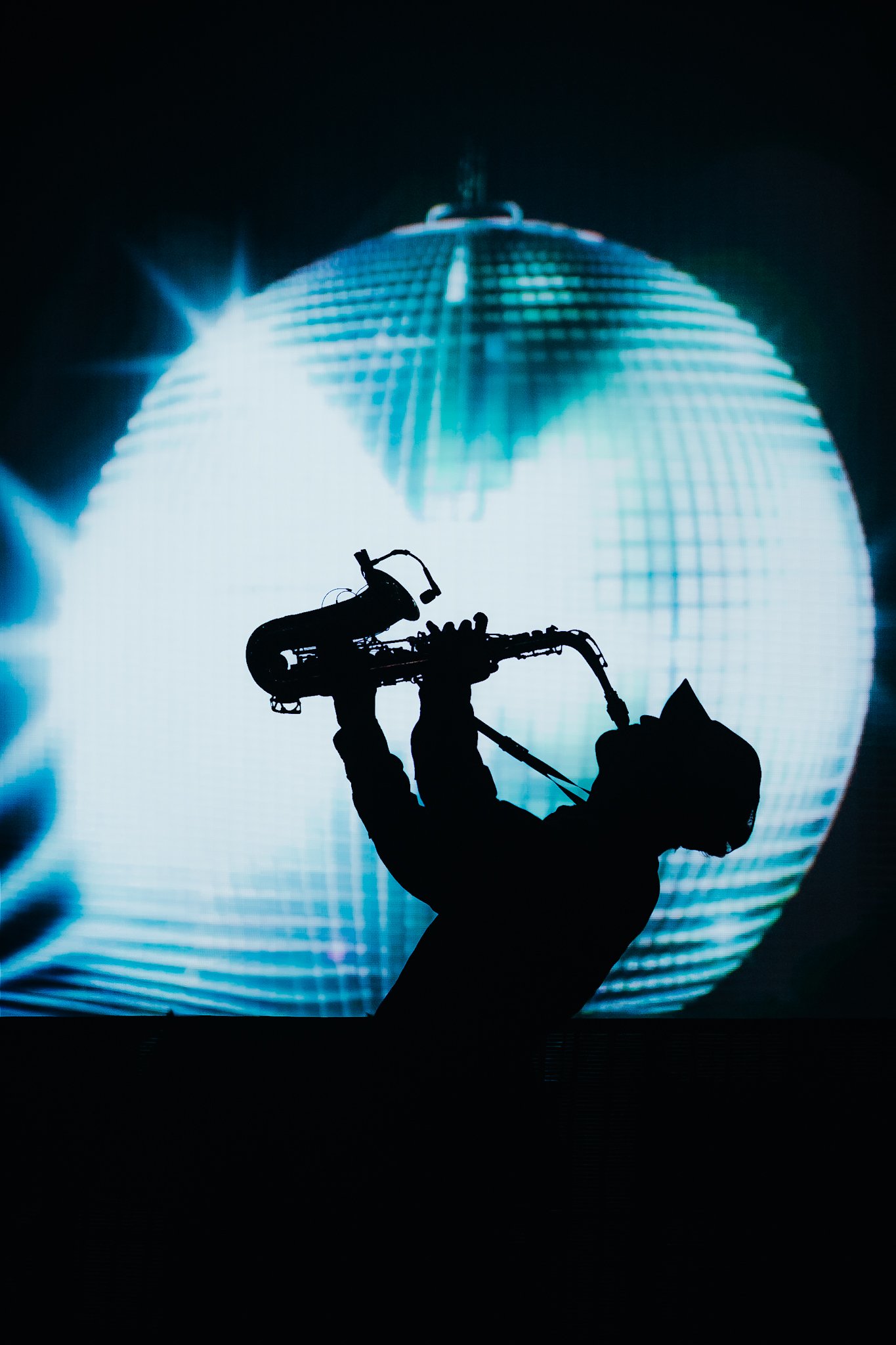 Silhouette of a person playing a saxophone, with a large illuminated disco ball in the background creating a dramatic effect.